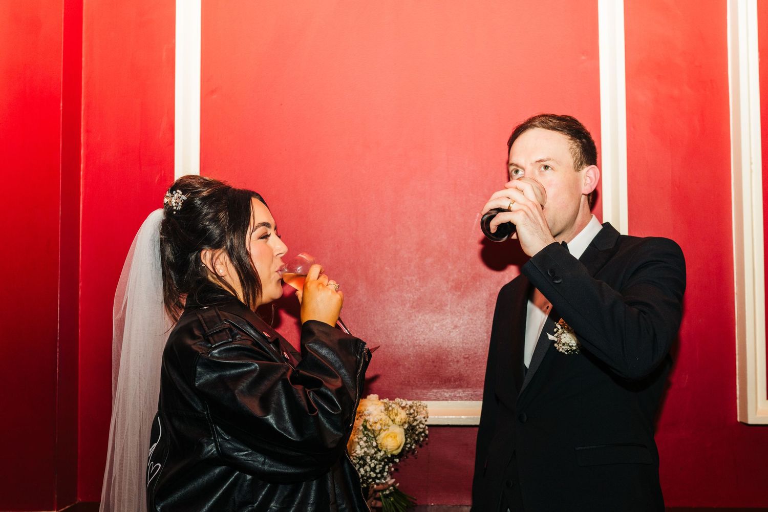 A wedding couple shares a joyful moment against a vibrant red wall background. Wedding PHOTOGRAPHER Dublin