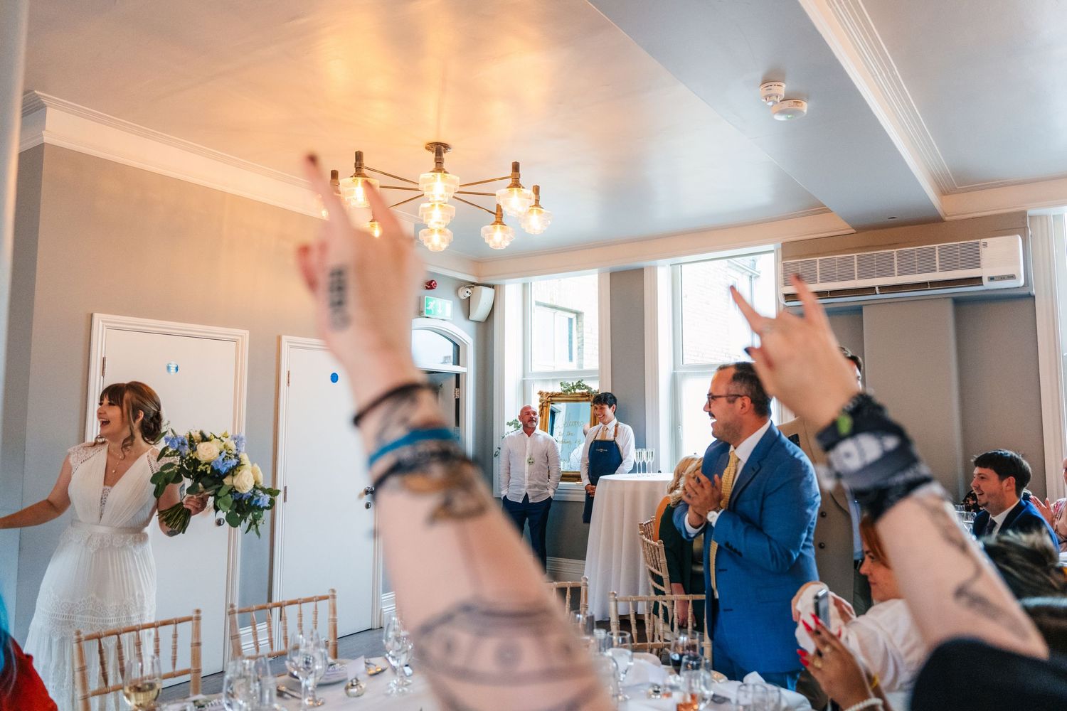 Wedding reception guests raise their hands in celebration during a toast at an indoor venue. PHOTOGRAPHER Dublin Ireland Wedding
