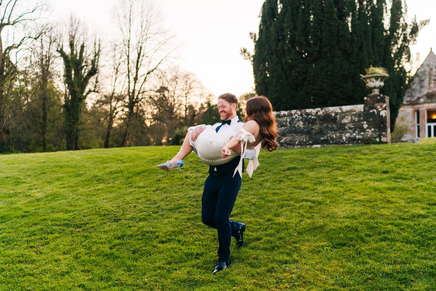 Castle Leslie Wedding Photographer Dublin Wedding couple playfully runs together on grassy hillside during outdoor spring photoshoot.