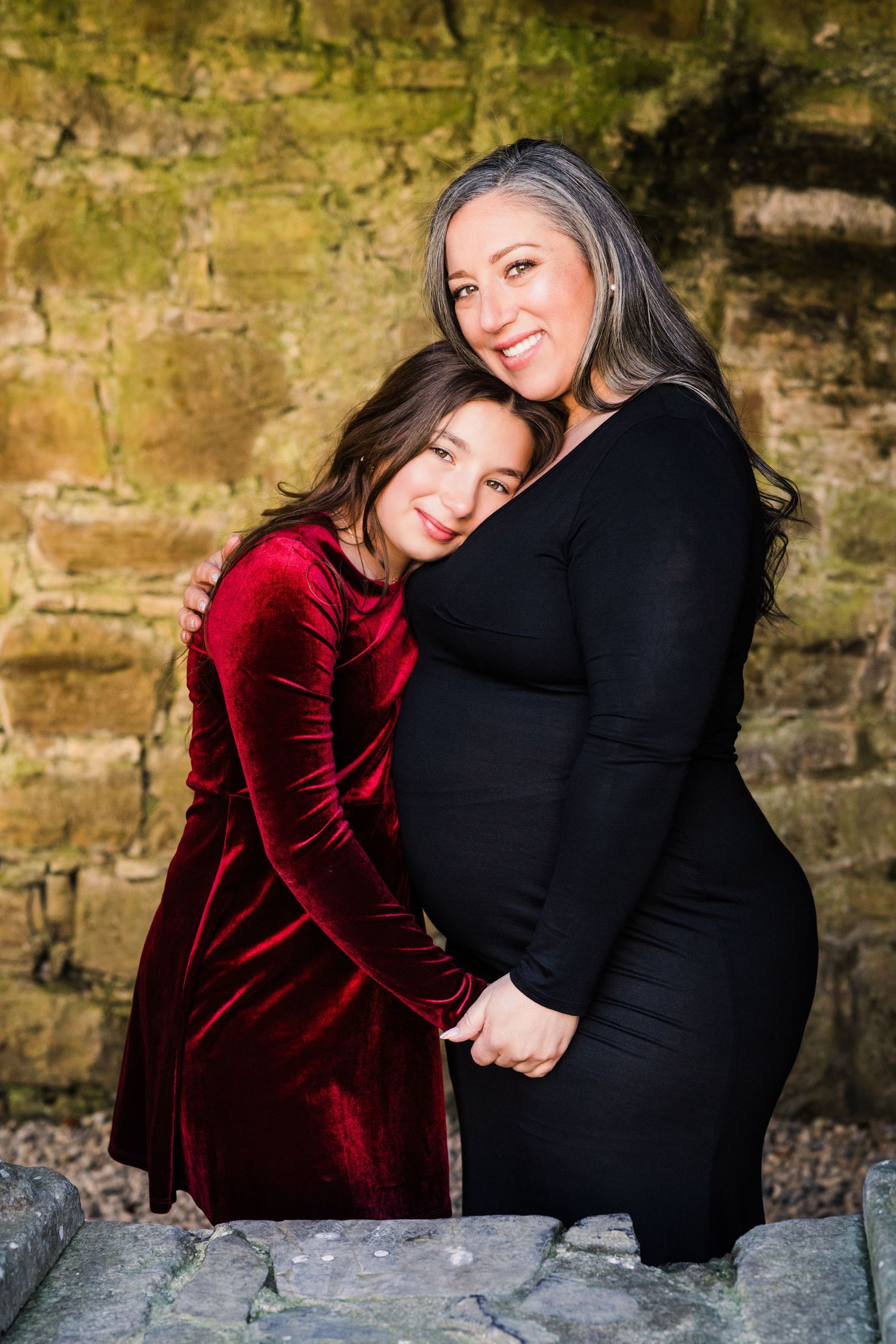 Two people share an intimate embrace while wearing red velvet and black dresses against a stone wall. Family PHOTOGRAPHER Dublin
