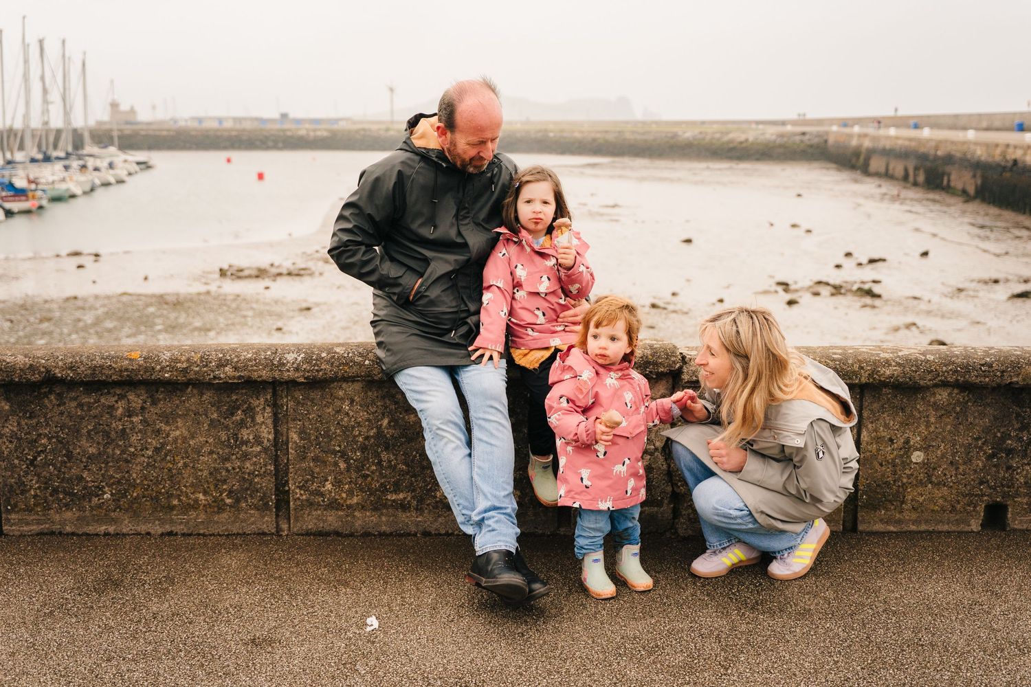 Family sitting together on stone wall at waterfront during overcast day. PHOTOGRAPHER Dublin