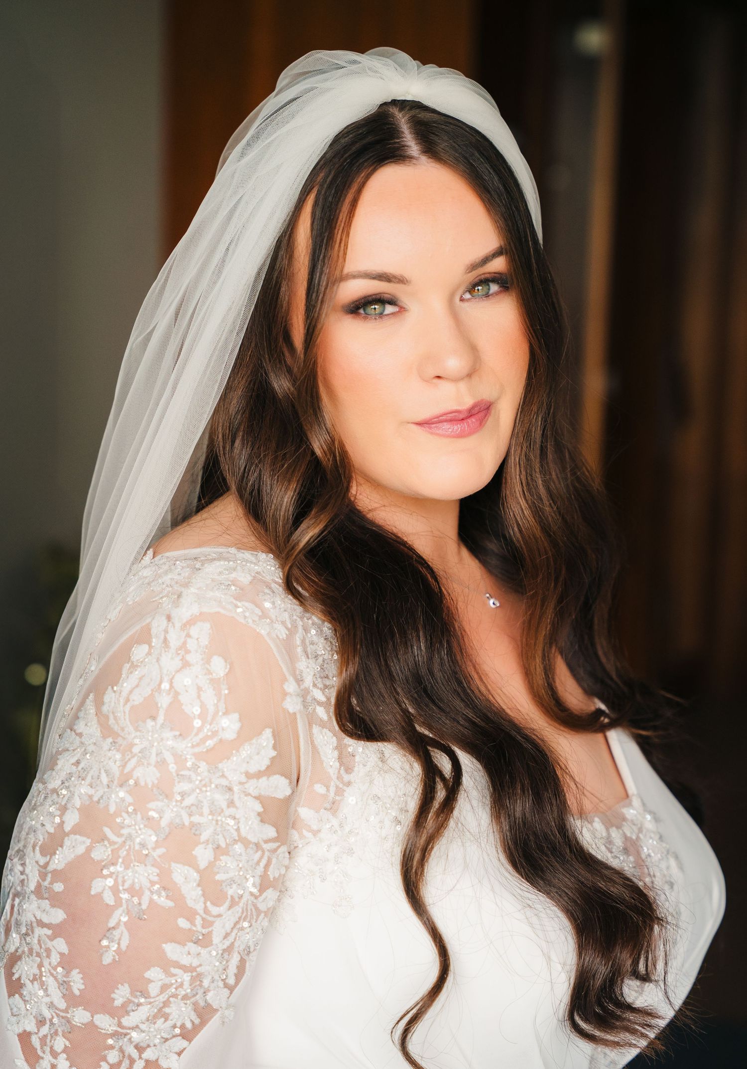 A bride wearing a white lace long sleeve wedding dress and veil poses indoors in elegant bridal portraits. Portmarnock Hotel Wedding PHOTOGR