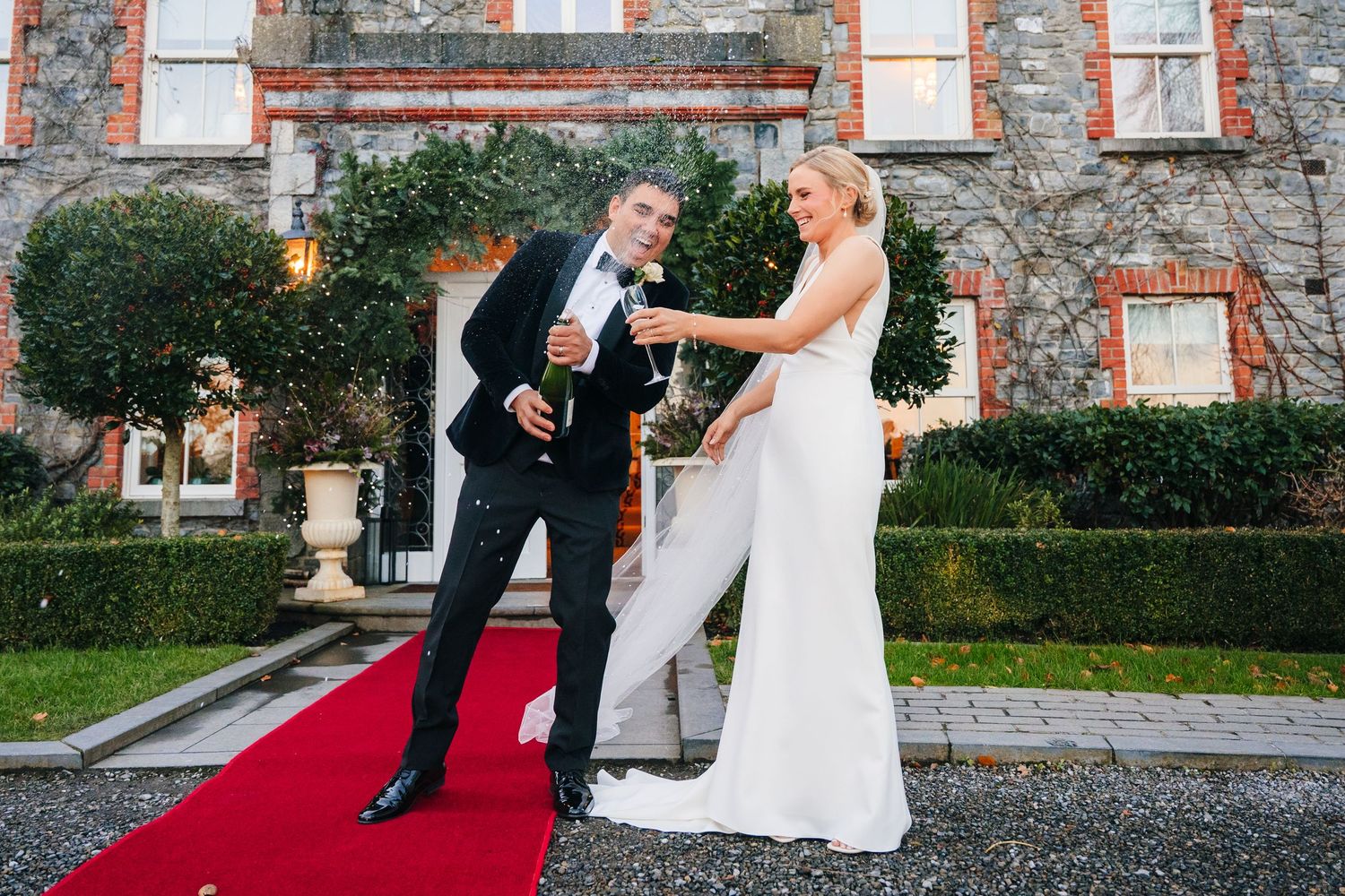 Newlyweds dancing and laughing together on a red carpet outside a stone building. Ballymagarvey Wedding photographer