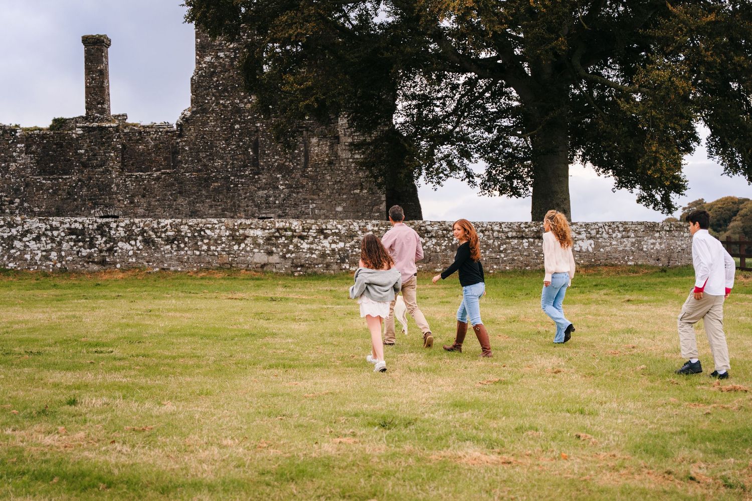 Group playing and running on grass near ancient stone ruins on a sunny day. BEctive abbey family photographer dublin