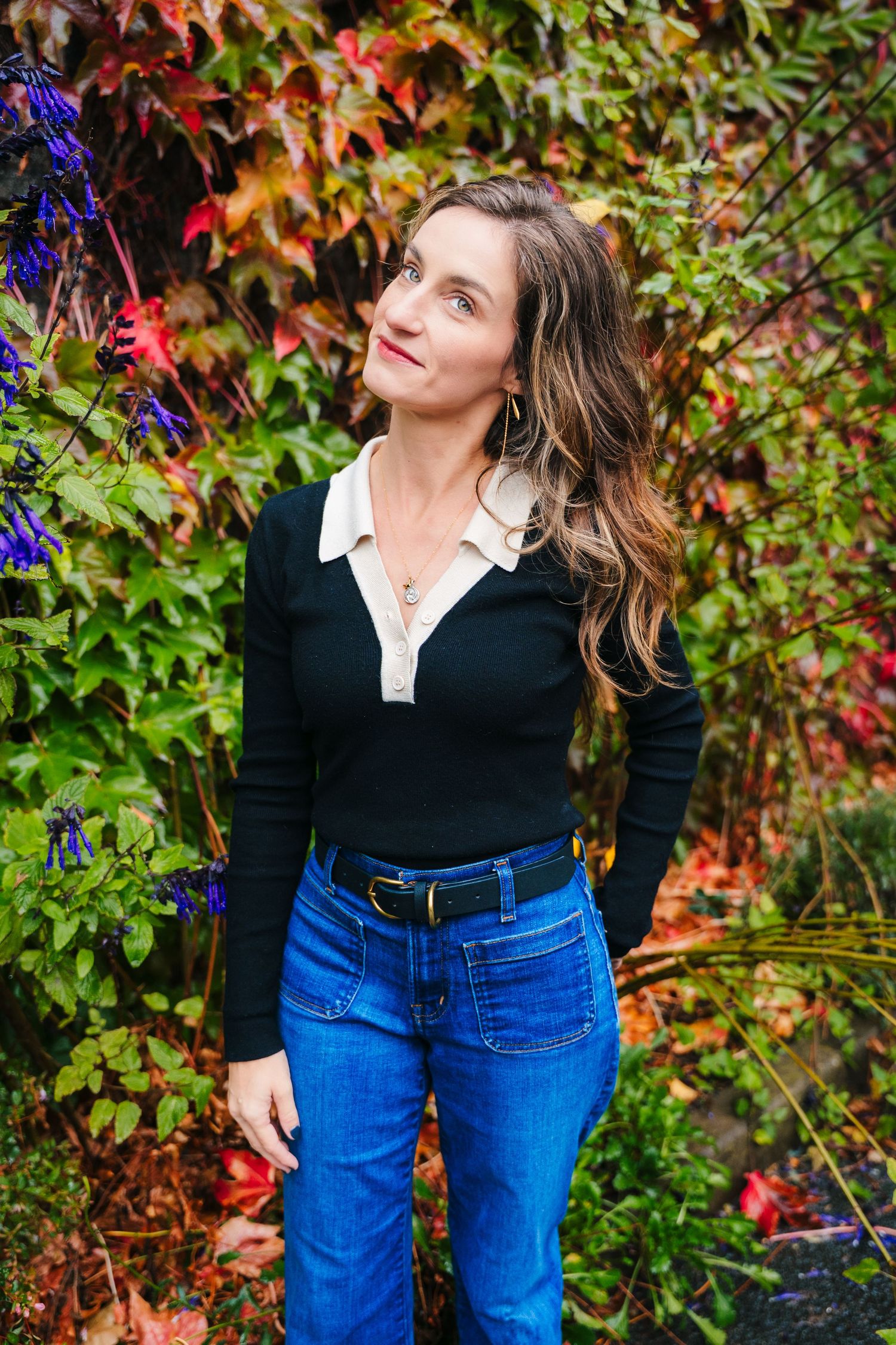 Person in casual fall outfit of black sweater and blue jeans poses against colorful autumn foliage background. professional headshots dublin
