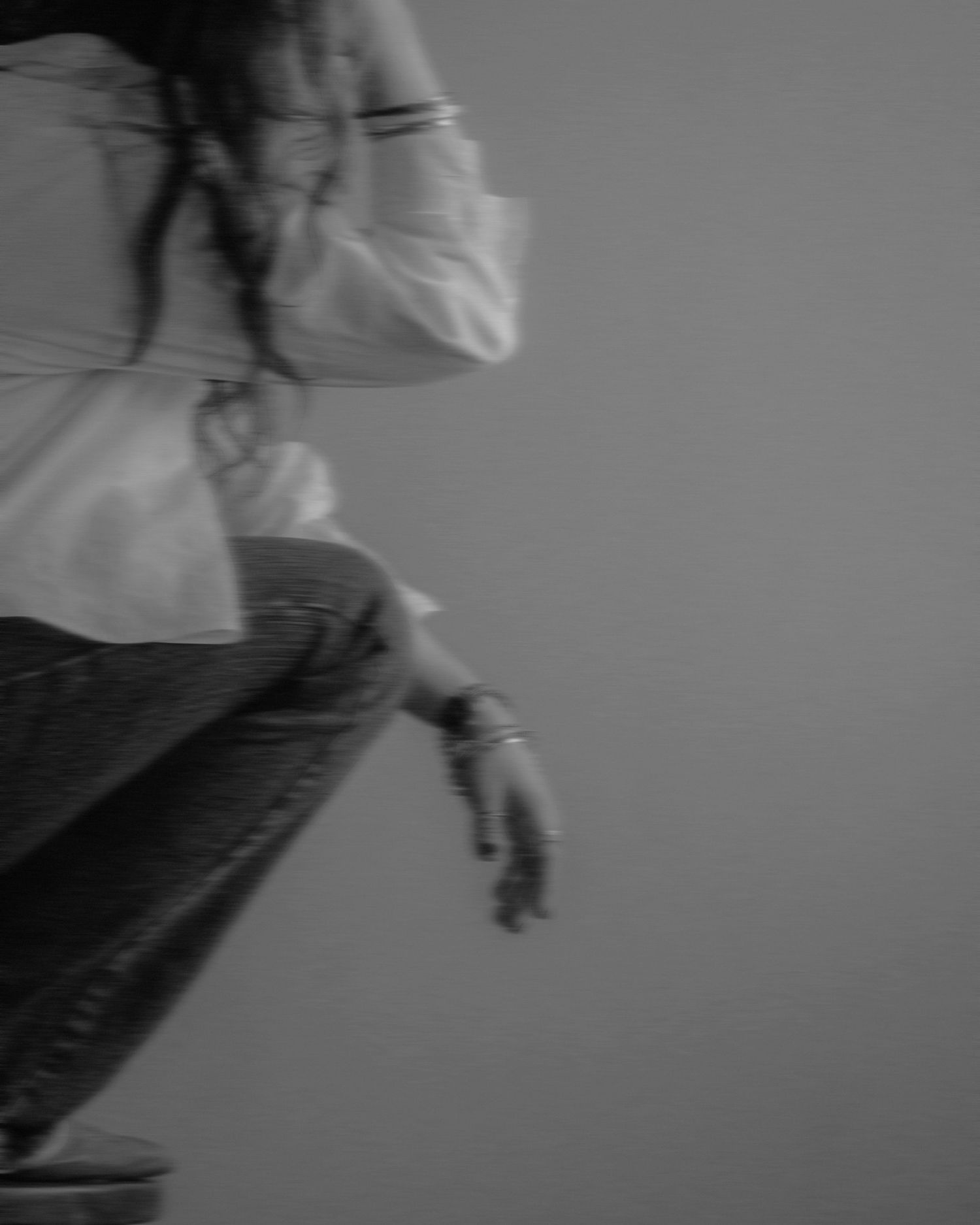 Artistic black and white photo showing motion blur of a person in jeans and white top walking with hand extended.