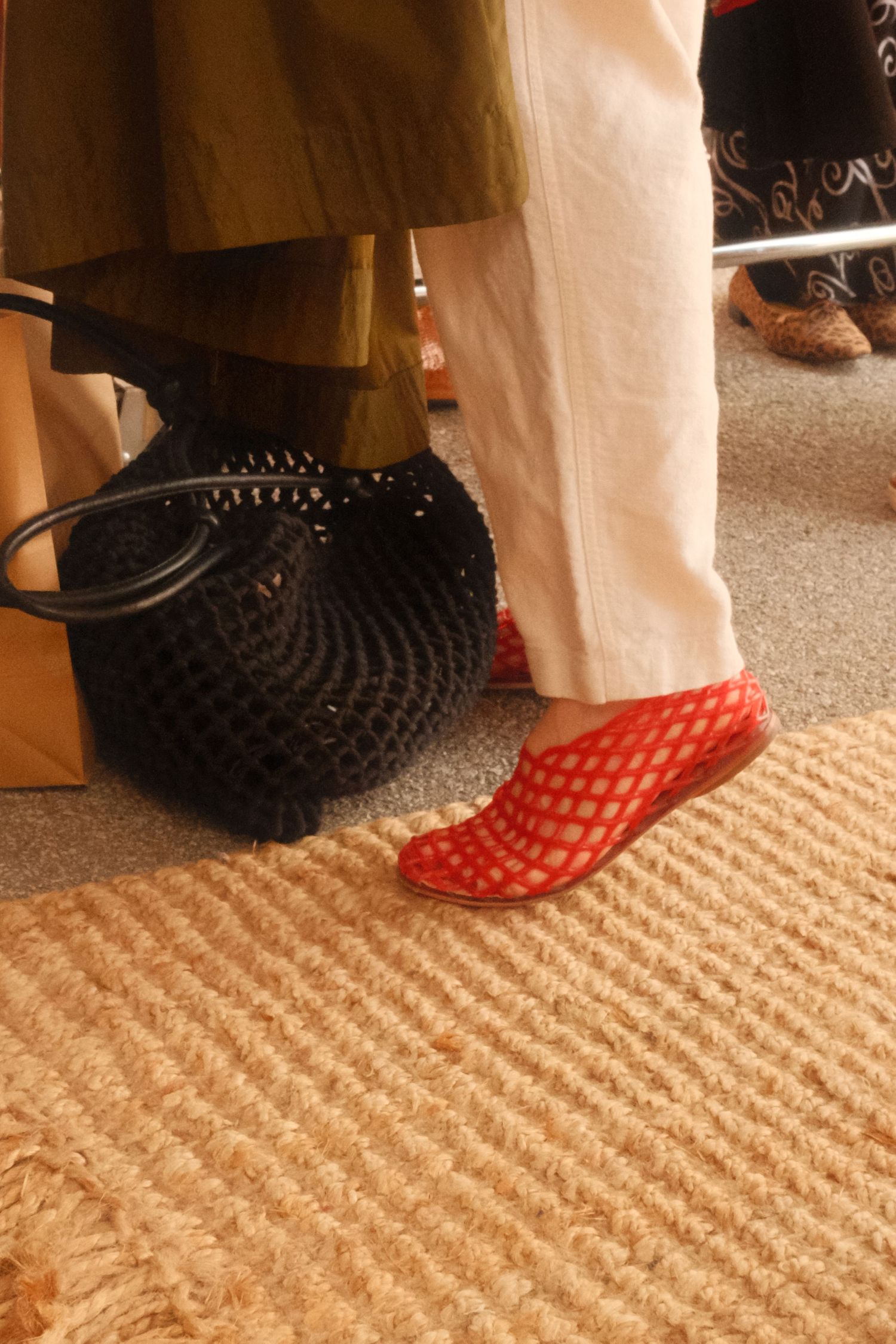 Red polka dot shoes and a black woven handbag sit on a beige textured carpet against white fabric.