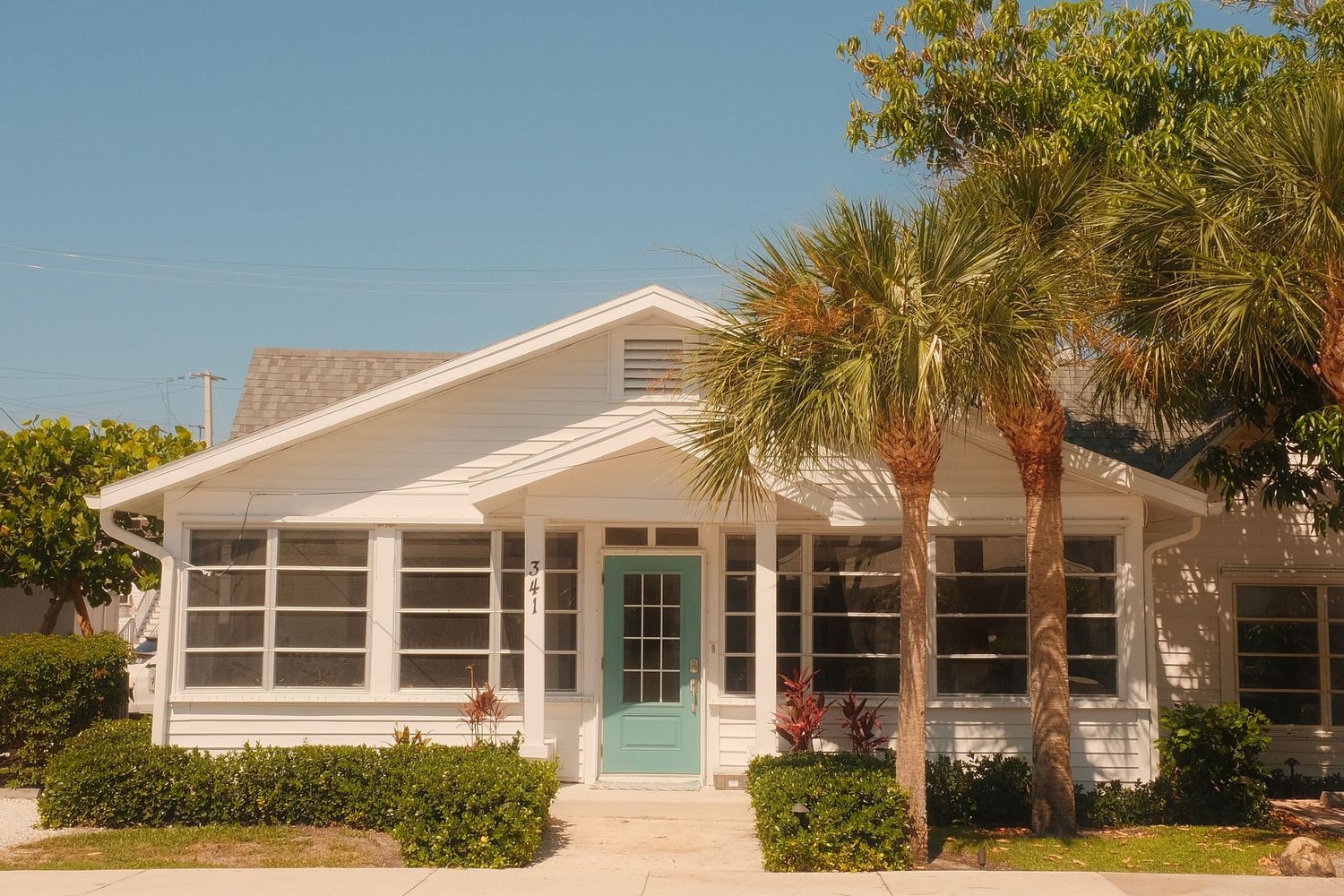 A series of beachfront houses with palm trees and white stucco exterior details line the coastal street.