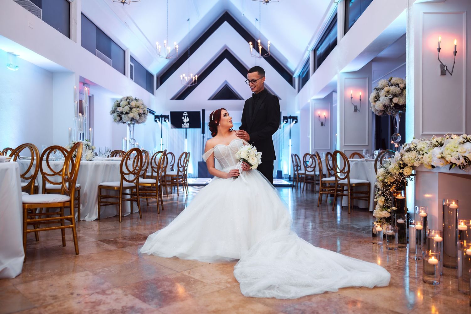 Elegant wedding venue with white walls, chandeliers, and a flowing bridal gown displayed in a spacious ballroom setting.
