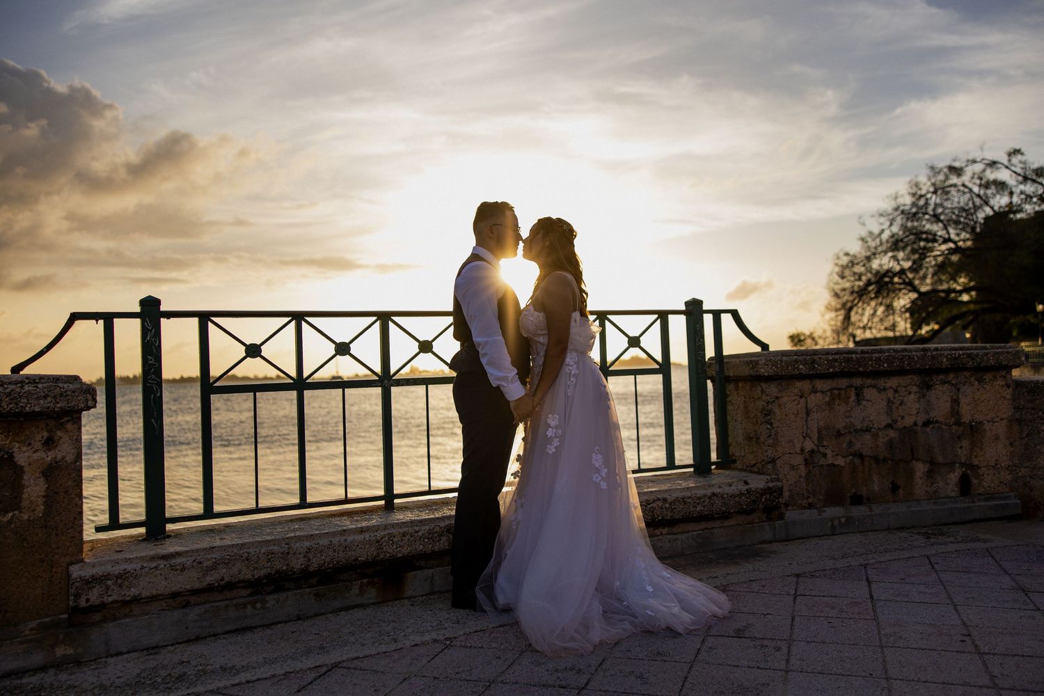 A couple watches a beautiful sunset from a patio overlooking the ocean.