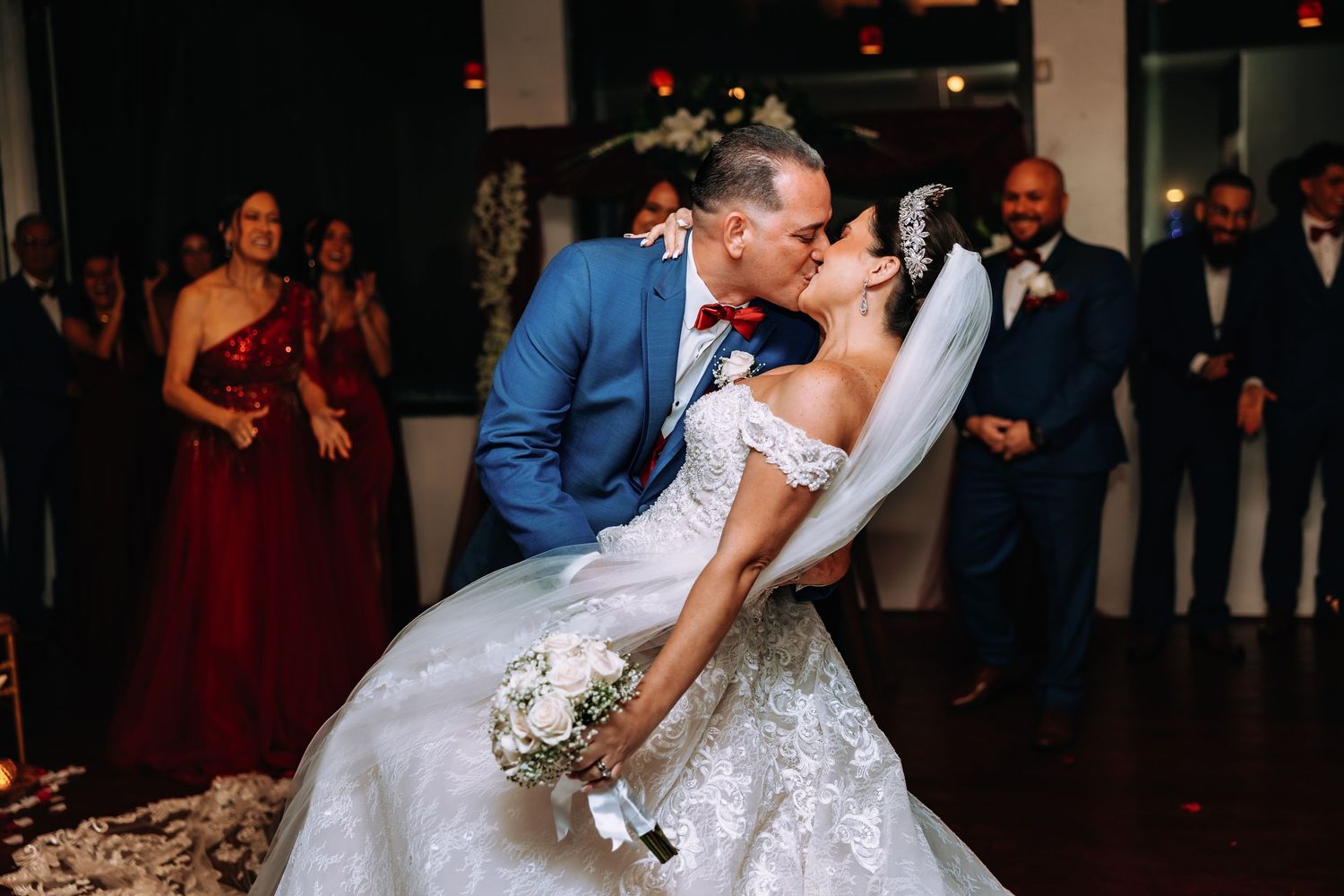 Bride and groom share romantic dip kiss on wedding dance floor surrounded by guests in elegant venue.