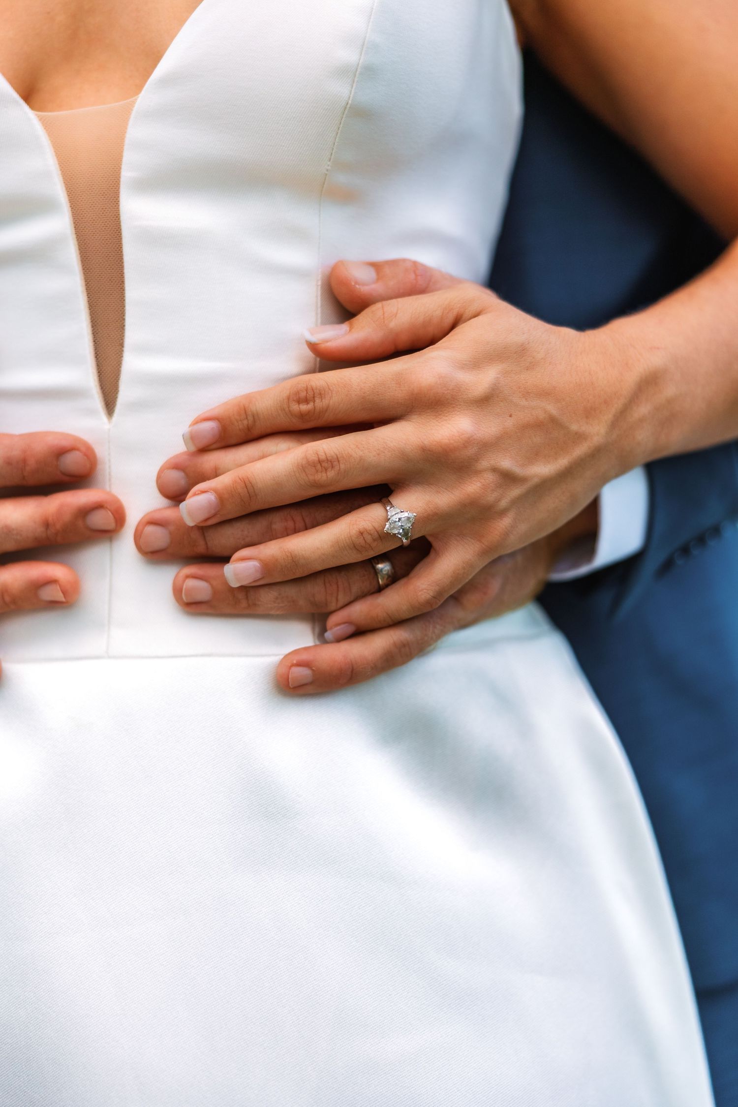 Close-up of bride and groom hands embracing, showcasing a sparkling diamond engagement ring on wedding day.