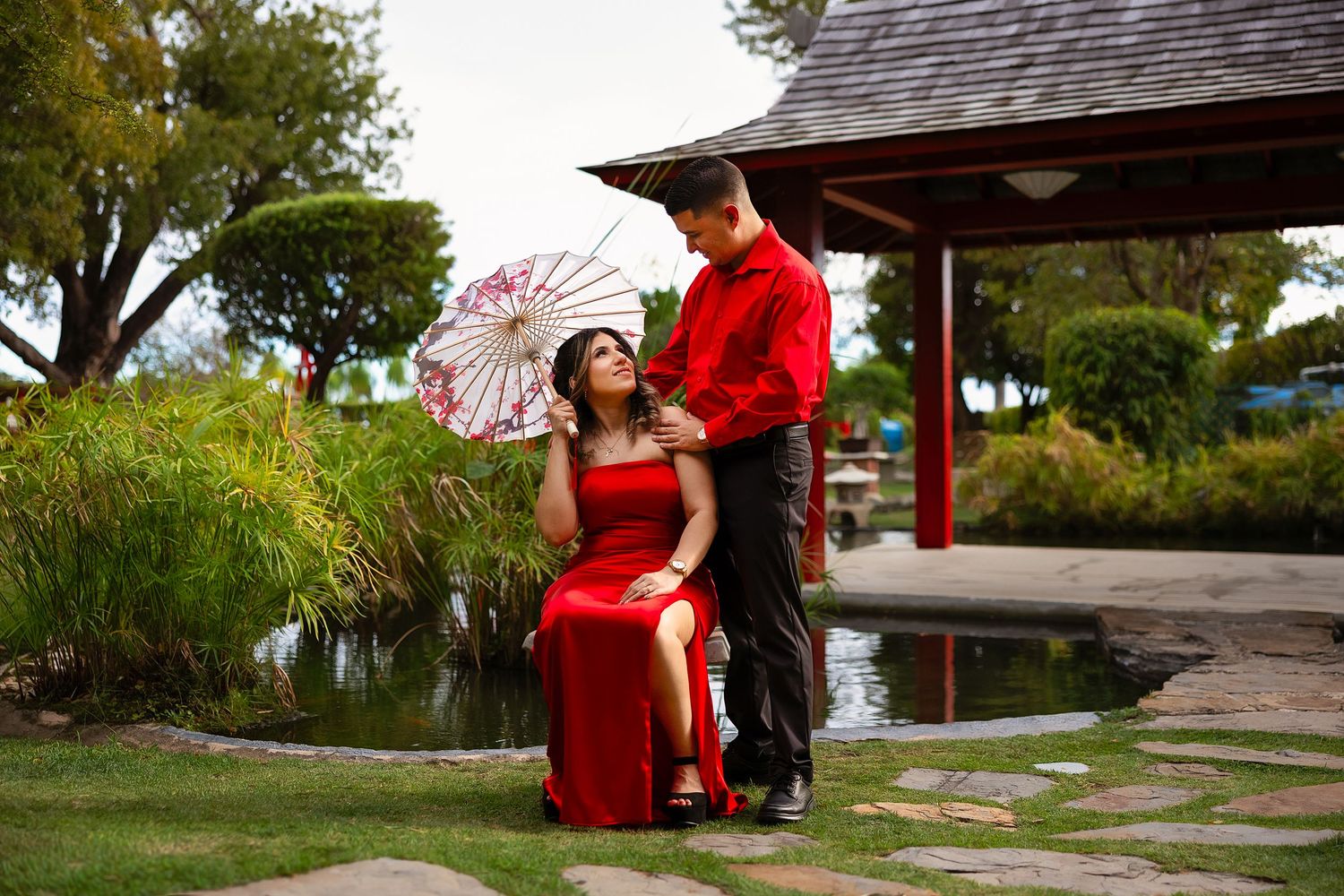A scenic garden walkway features stone pavers leading to a red Japanese-style pavilion on a peaceful summer day.