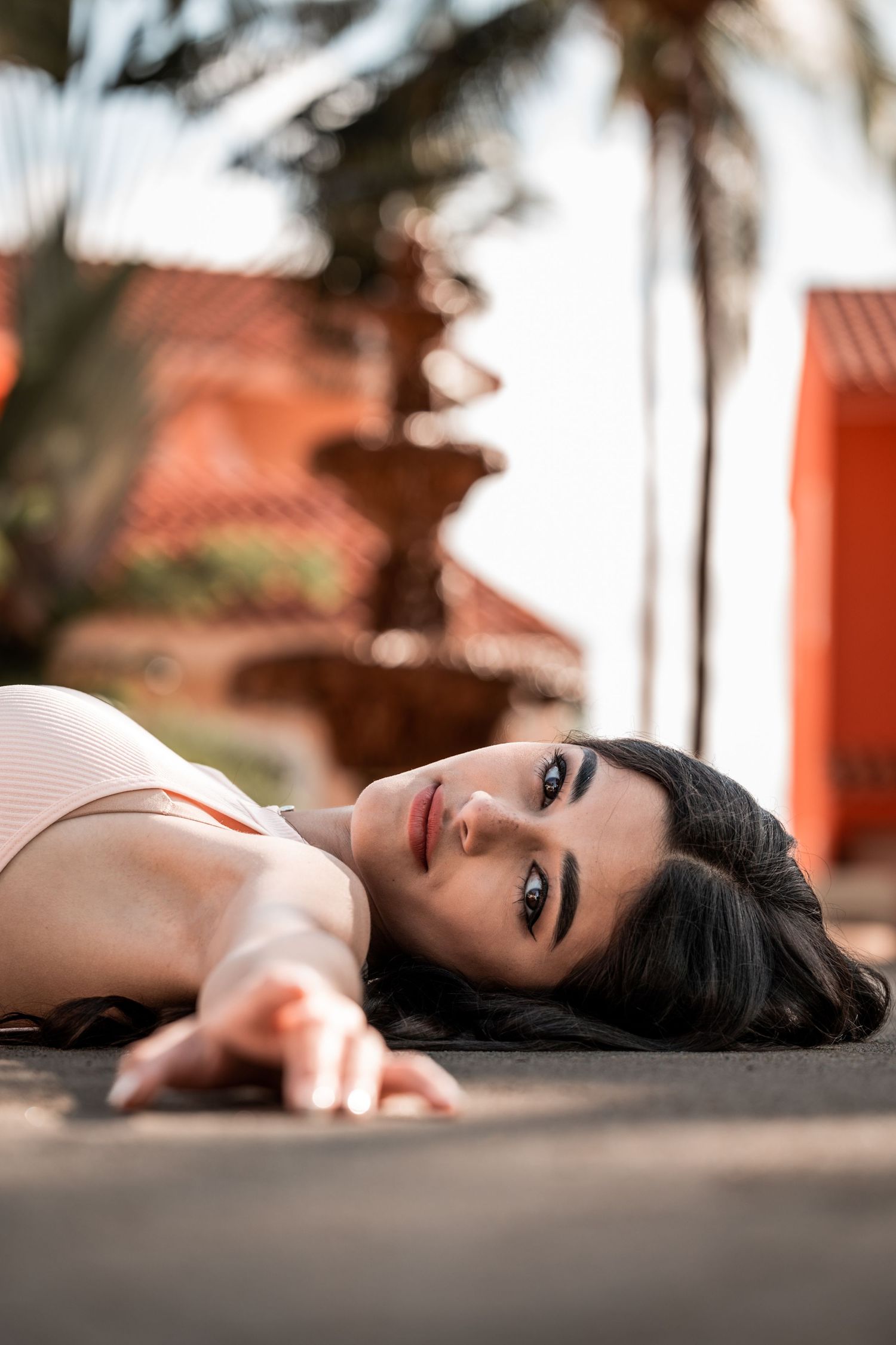 A person lying on the ground with blurred palm trees and red building in the background.