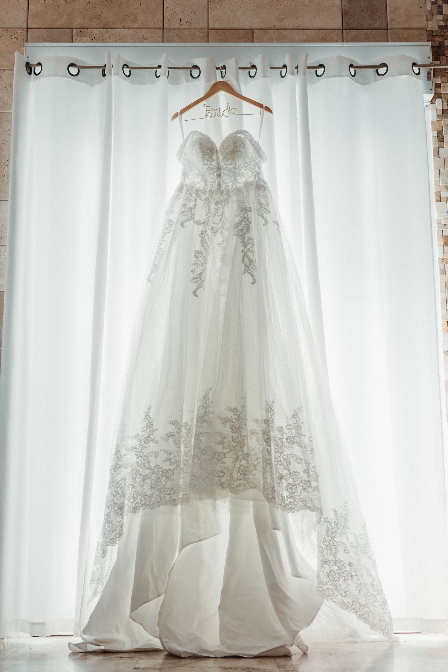Elegant strapless A-line wedding dress with lace floral details hanging on a wooden bridal hanger.
