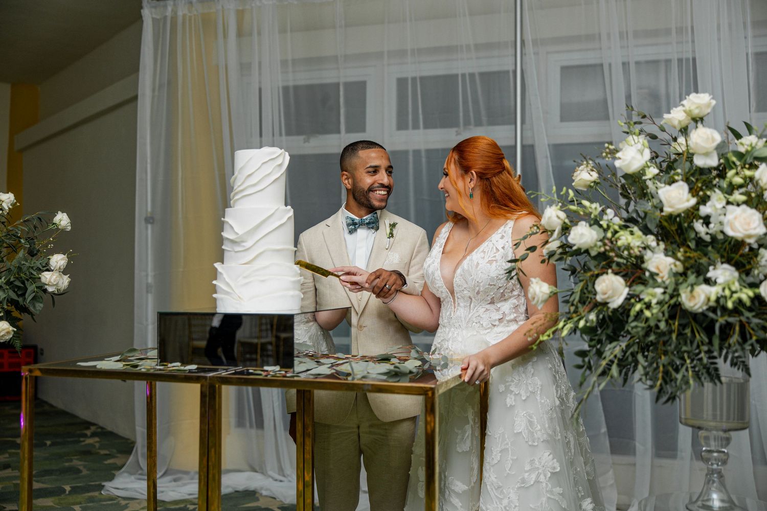 Smiling newlyweds cut their white wedding cake together at a beautifully decorated wedding reception.