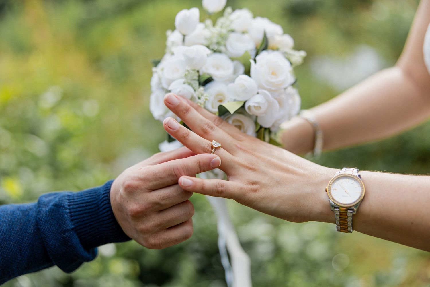 Close-up of hands exchanging rings during a wedding ceremony with white floral bouquet in the background.