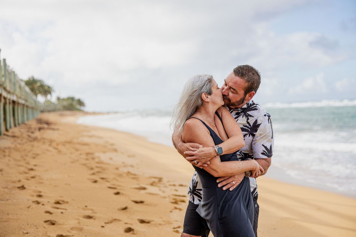 A romantic beach wedding photoshoot with waves crashing in the background on a cloudy day.