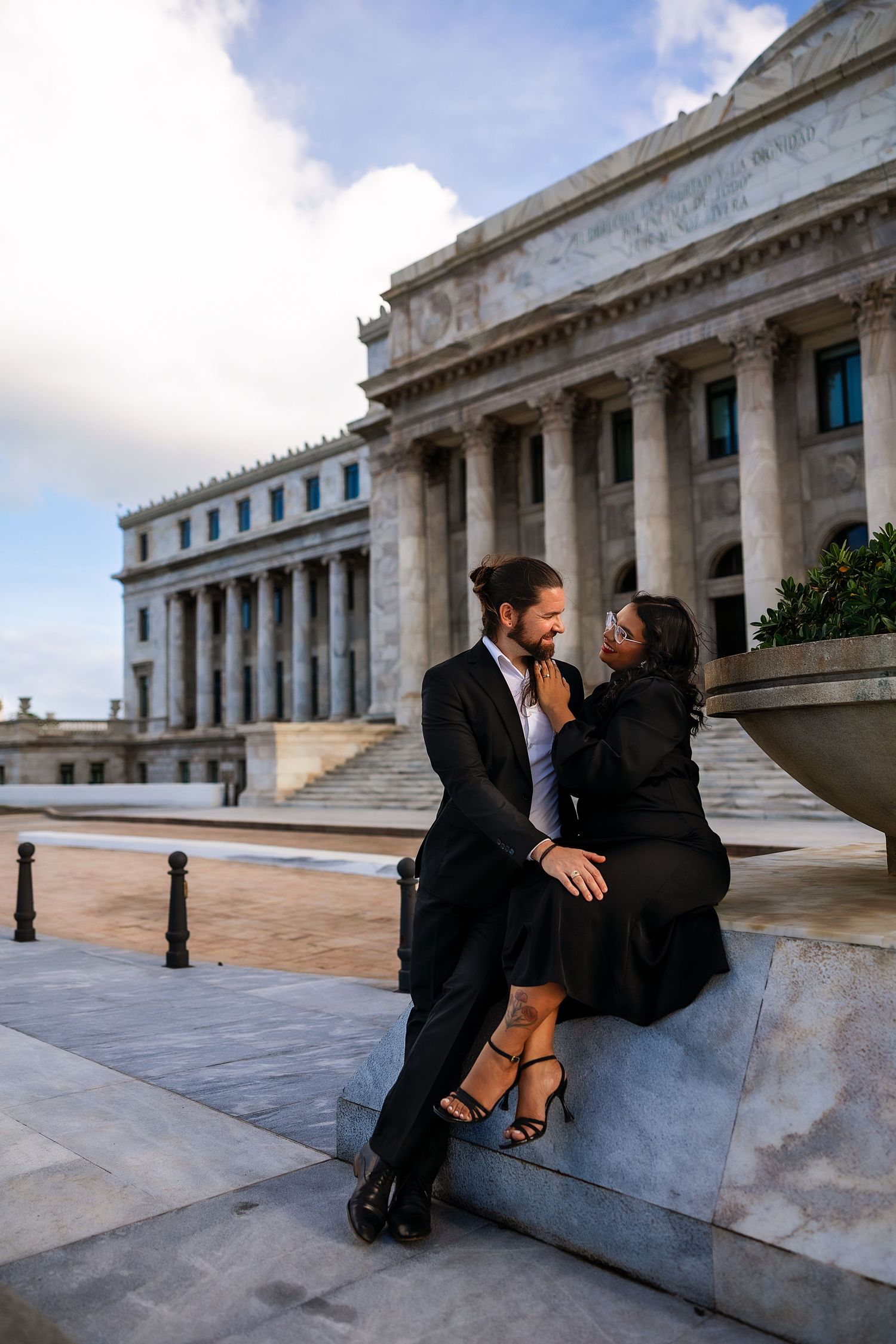 A couple in formal attire shares a romantic moment on the steps of a grand neoclassical building with columns.
