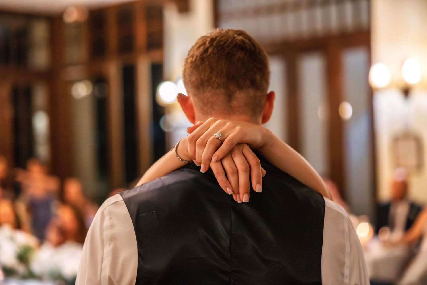 Couple sharing a slow dance embrace at a wedding reception, woman's hand resting on man's shoulder.
