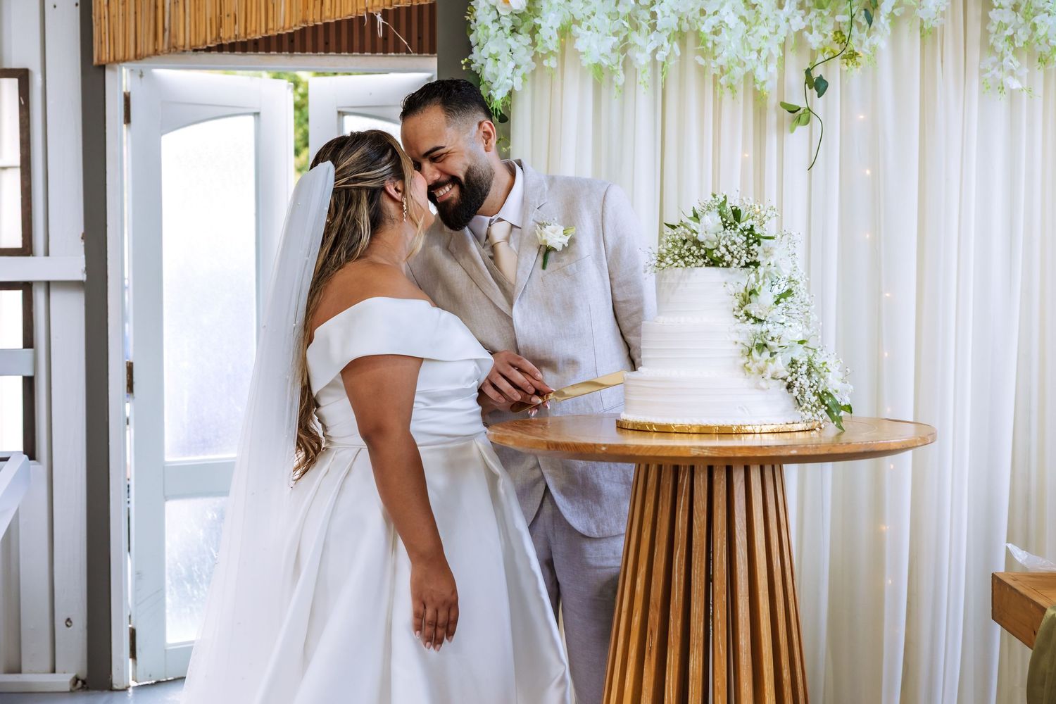 Bride and groom cutting white wedding cake together at elegant floral decorated venue.