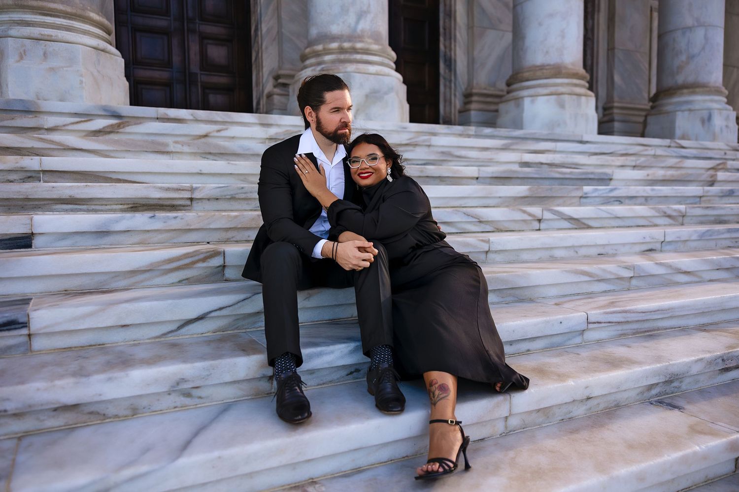 Romantic couple embracing on marble steps outside a classical building with tall stone columns.
