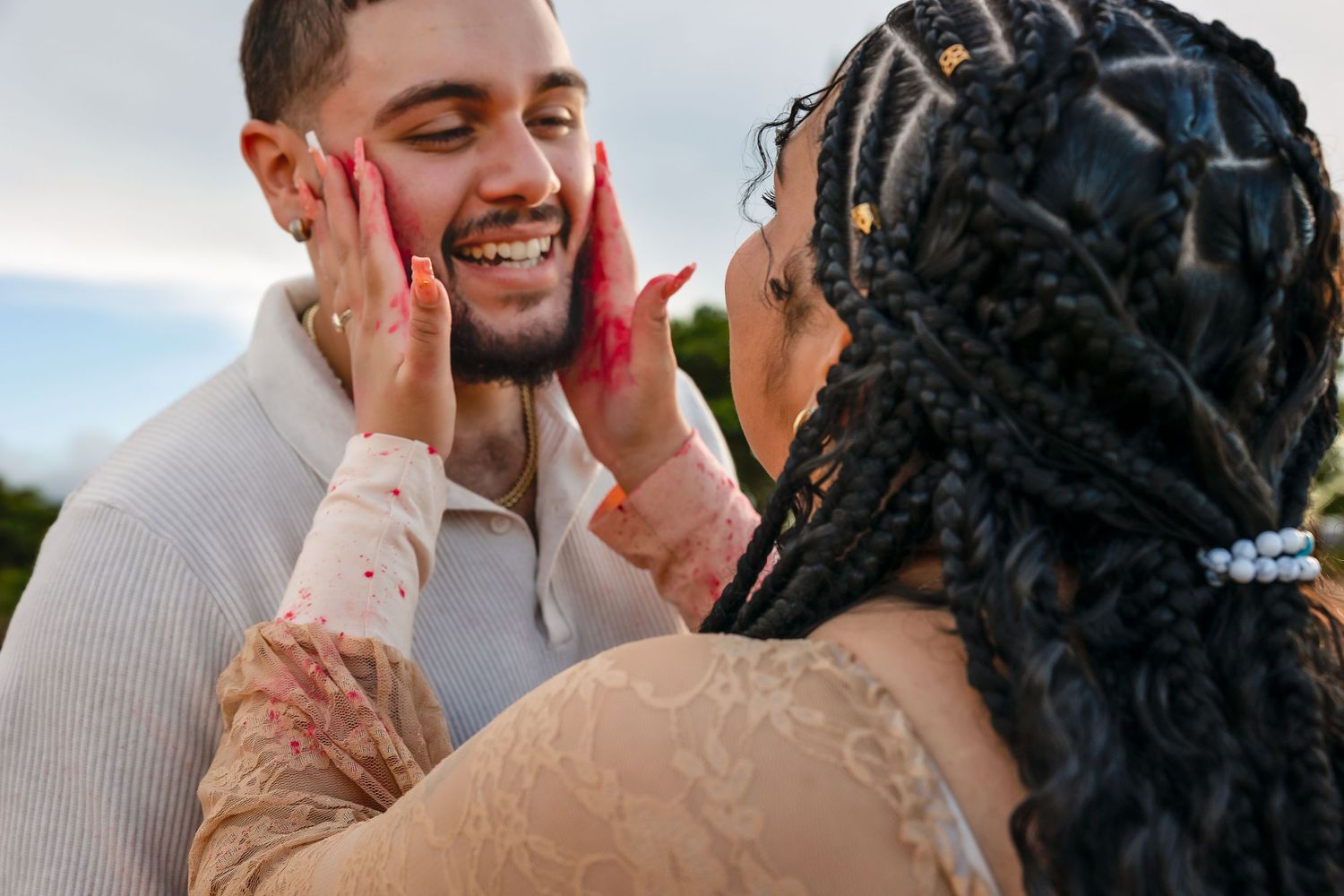 A joyful couple shares a tender moment, the woman with braids holding her partner's face with henna-painted hands.