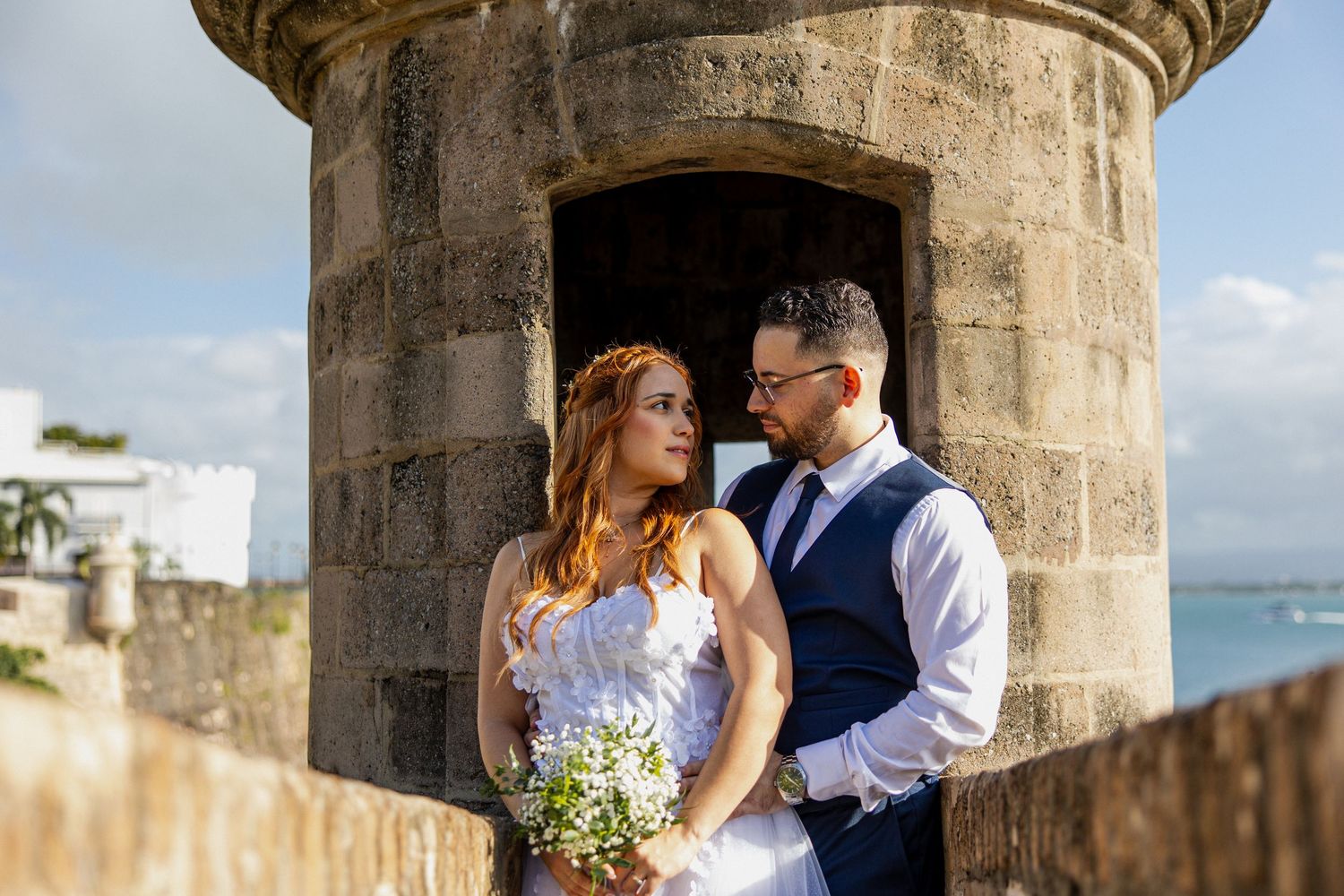 Bride and groom share a romantic moment by a stone fortress wall with ocean views in Old San Juan, Puerto Rico.