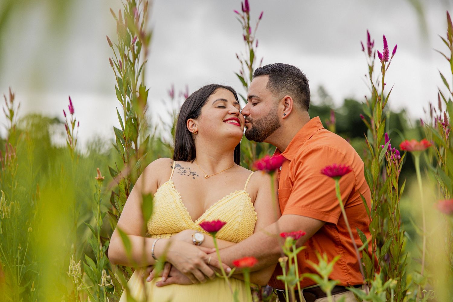 Couple sharing a romantic moment in a vibrant flower field, woman in yellow dress, man in orange shirt.