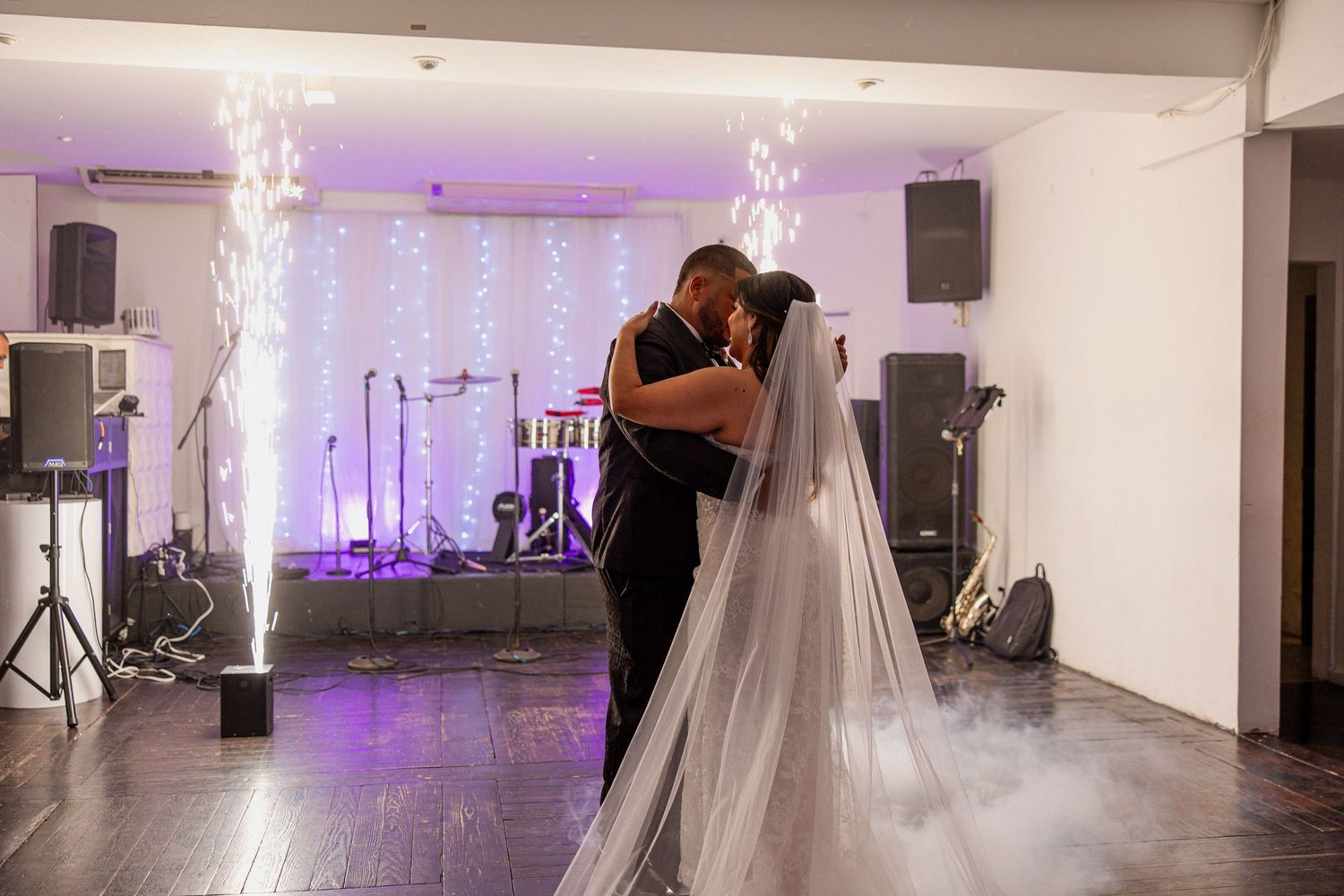 Bride and groom share first dance on foggy dance floor with purple lights and sparkling backdrop at wedding reception.