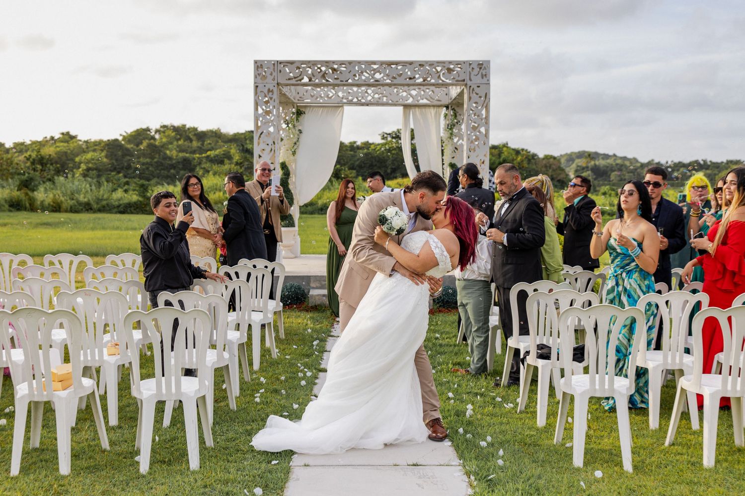 Outdoor wedding ceremony setup with white chairs arranged in rows on a grassy lawn surrounded by trees and nature.