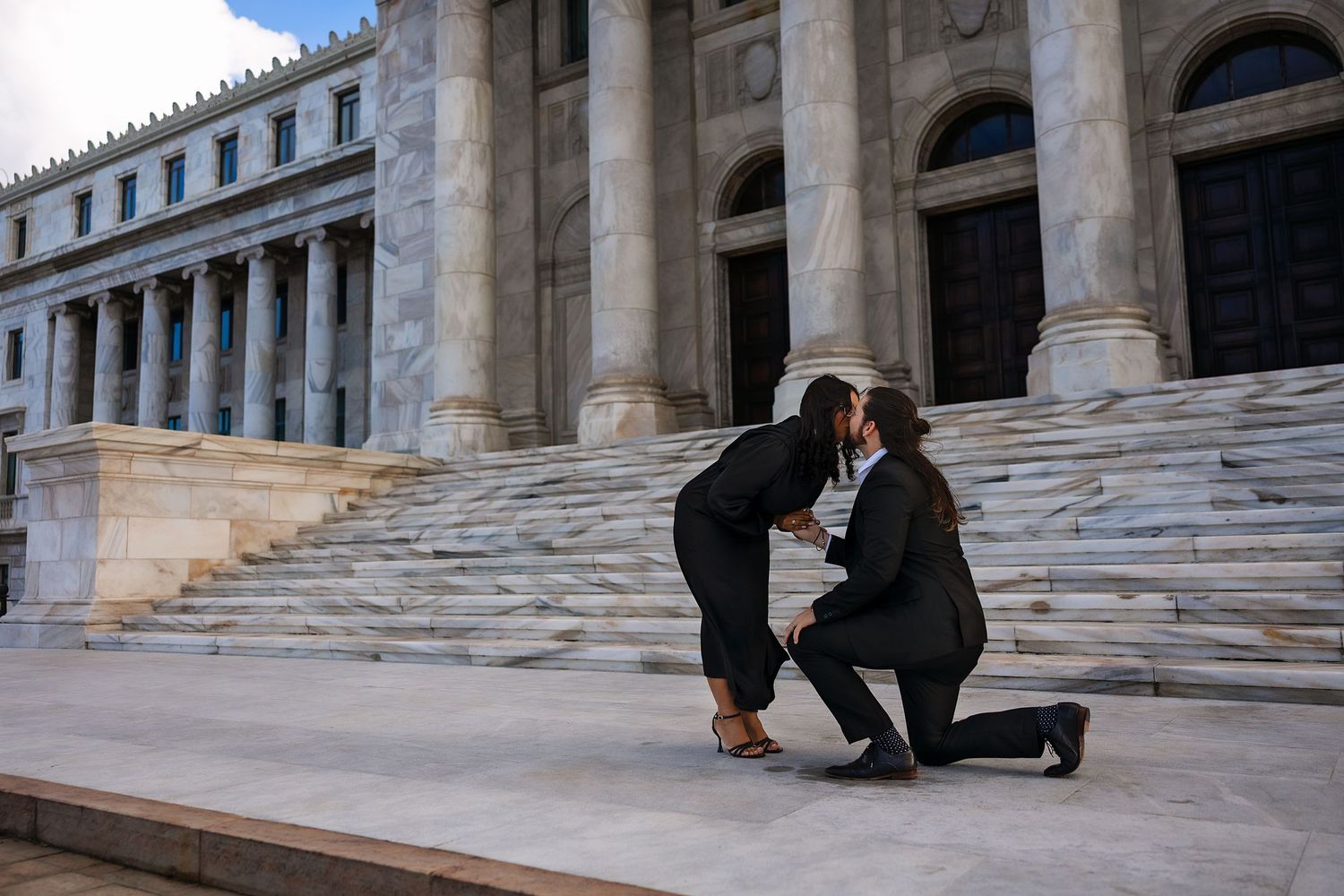 A couple in formal attire shares an intimate moment on elegant stone steps of a historic building.