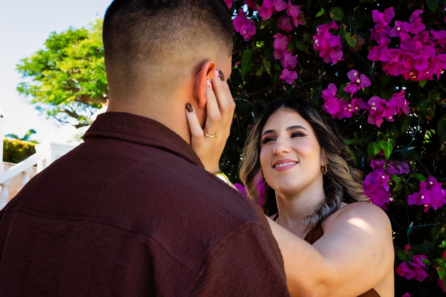 A romantic couple embraces under vibrant purple bougainvillea flowers in a garden setting.