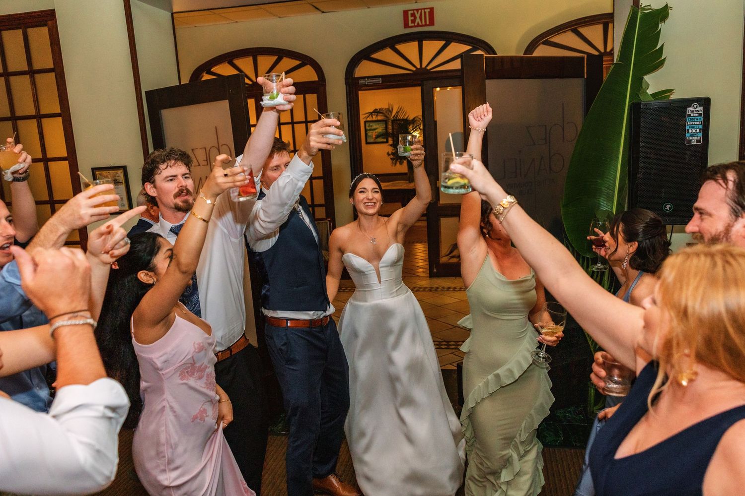Wedding couple celebrates with guests raising glasses in a joyful reception toast inside an elegant venue.