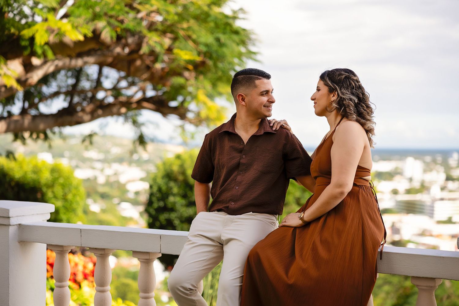 Romantic couple embraces and laughs together while sitting outdoors on a sunny day.