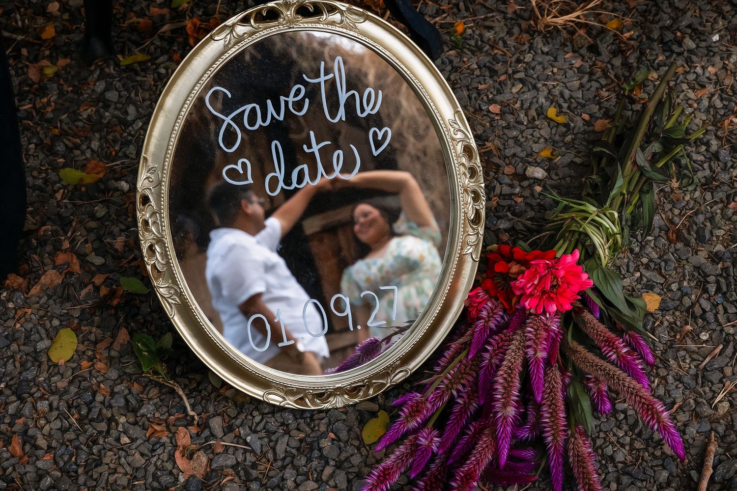 Save the date mirror sign dated 01.09.27 reflecting couple dancing, with red floral bouquet beside it.