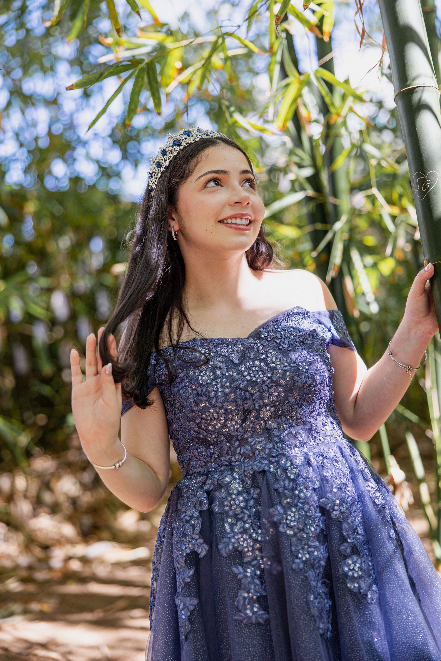 Woman in purple lace dress poses elegantly among bamboo plants.