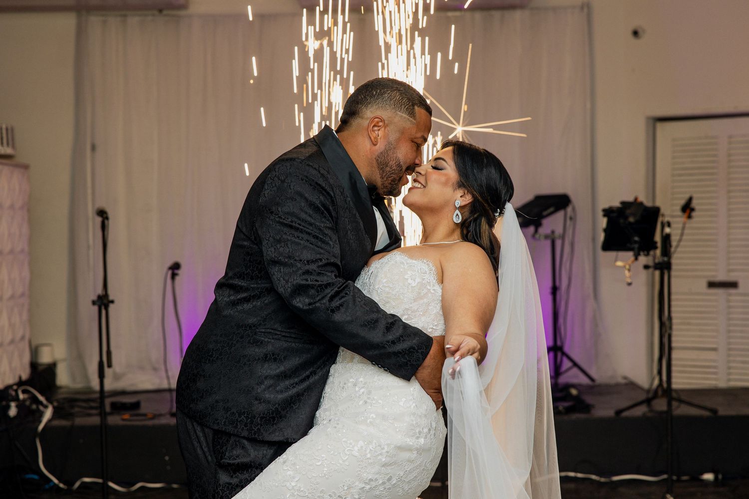 Bride and groom share romantic first dance kiss with sparkling fireworks backdrop at elegant wedding reception.