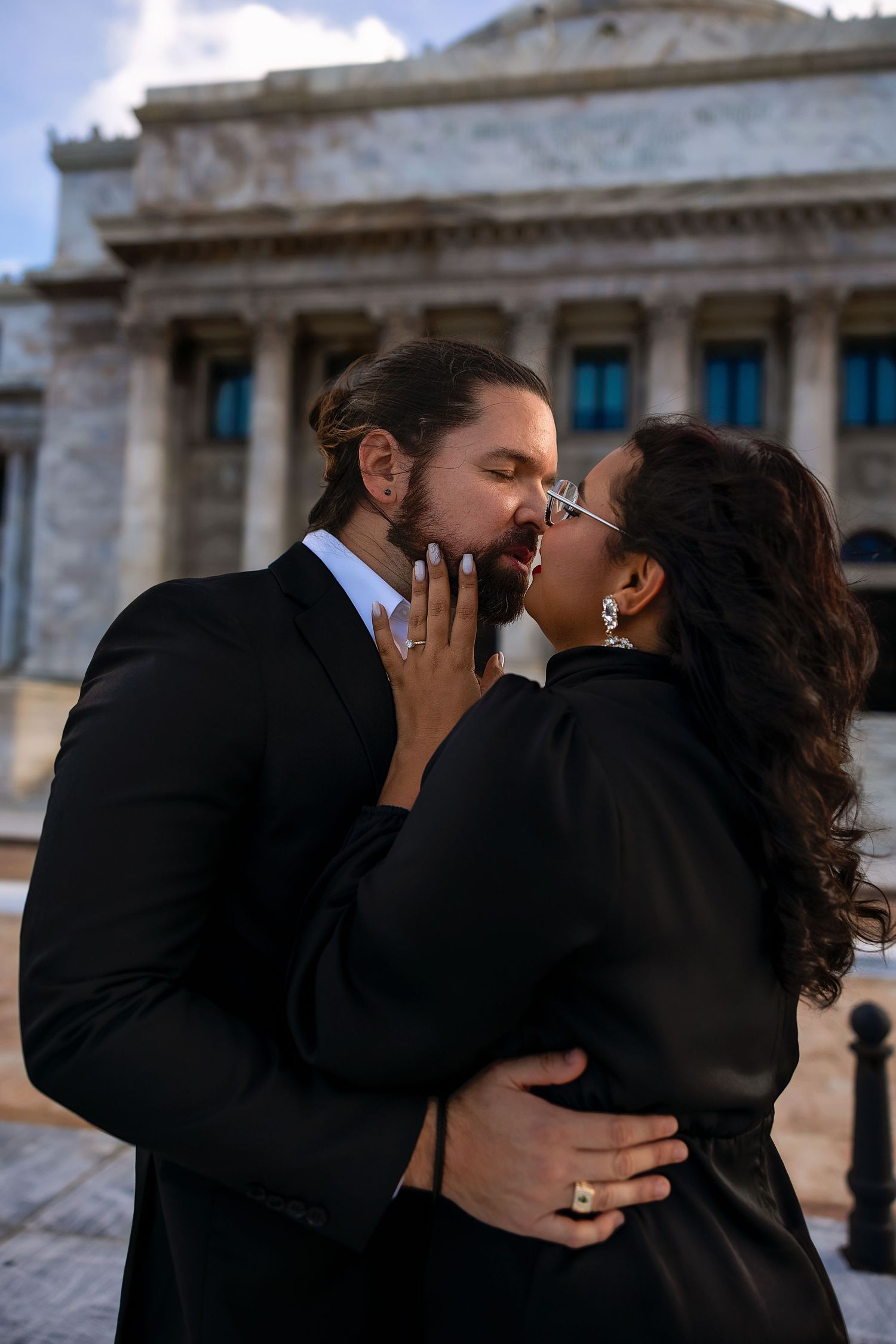 A couple shares an intimate kiss in front of a historic government building with ornate architecture.