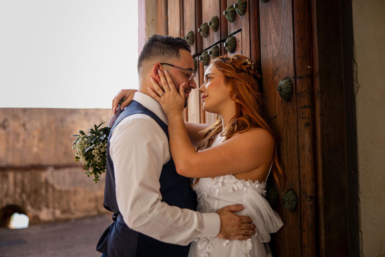 A romantic wedding moment captured against an antique wooden door in warm sunlight.