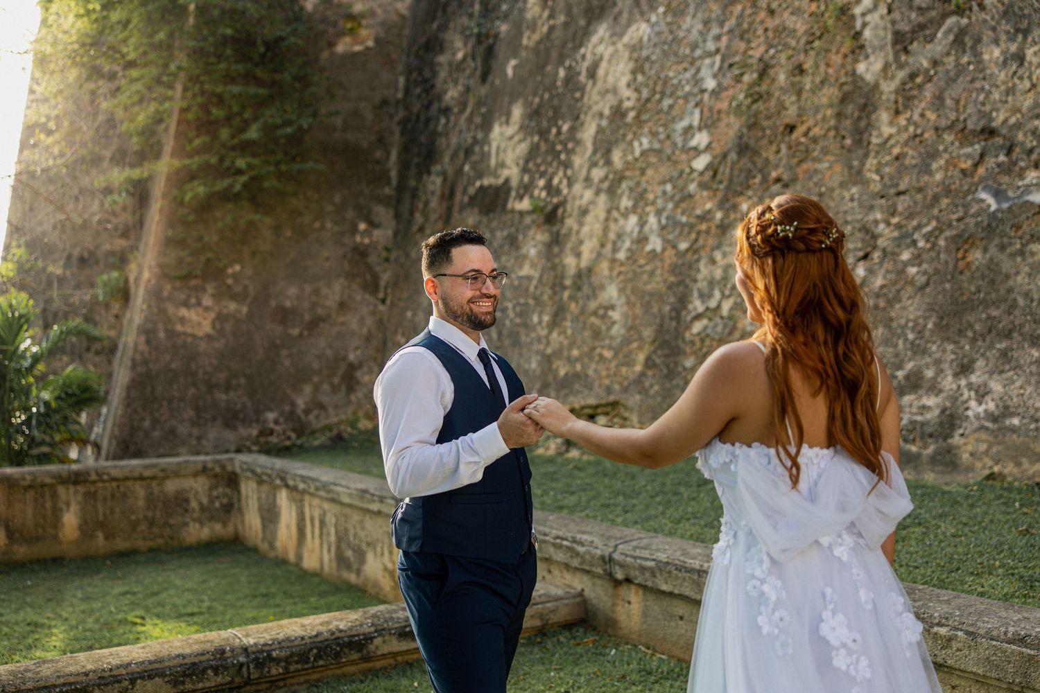 A couple shares an intimate moment against a stone wall backdrop during sunset.
