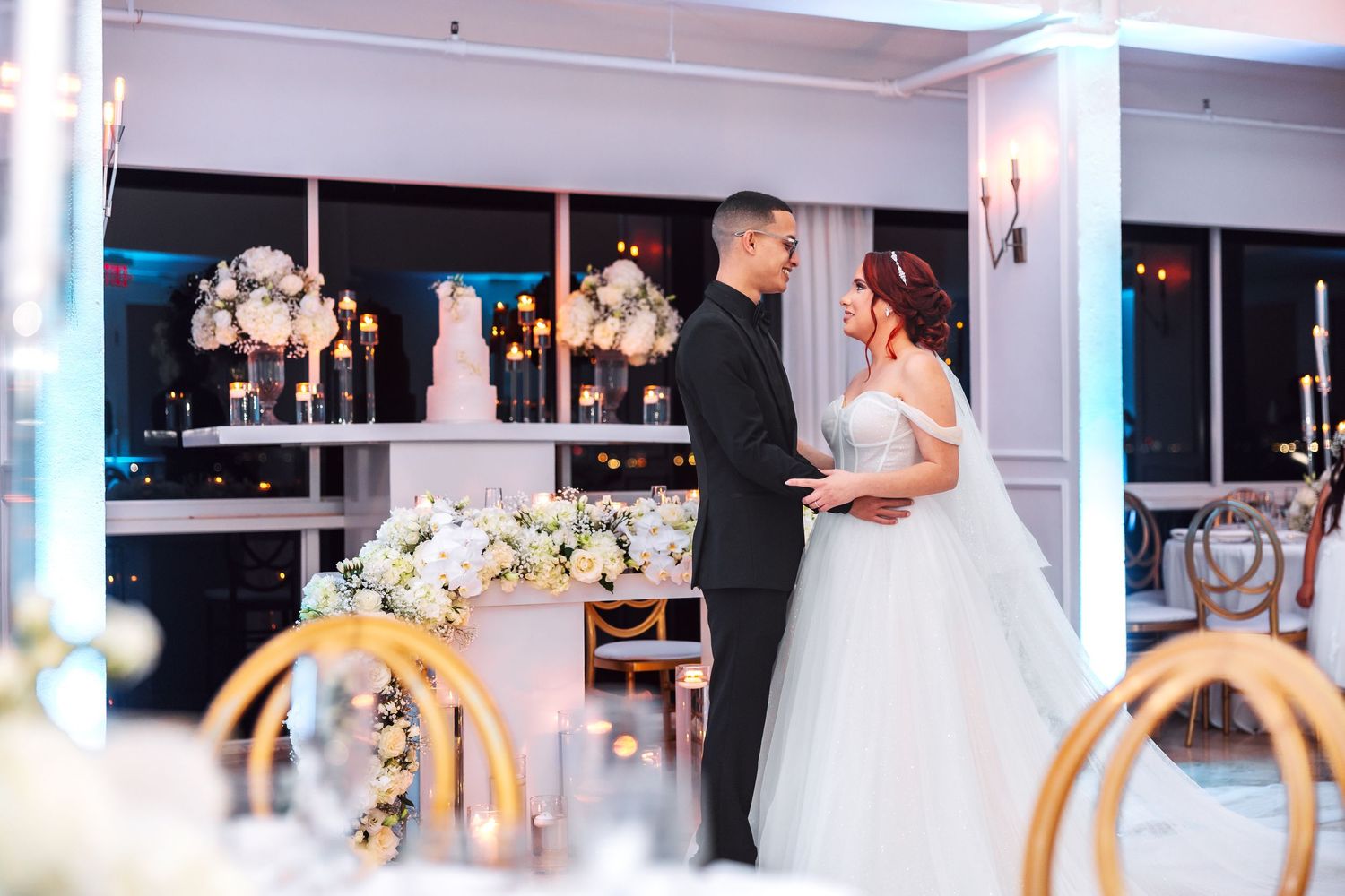 A panoramic view of a wedding reception venue with white decor, floral arrangements, and elegant table settings.