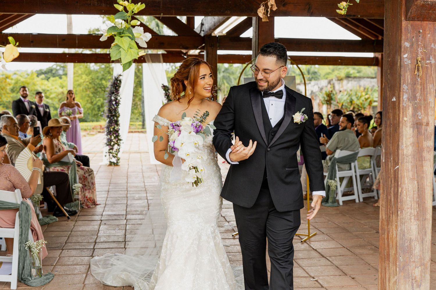 Bride and groom walk arm in arm down the aisle after wedding ceremony at an outdoor pavilion venue.