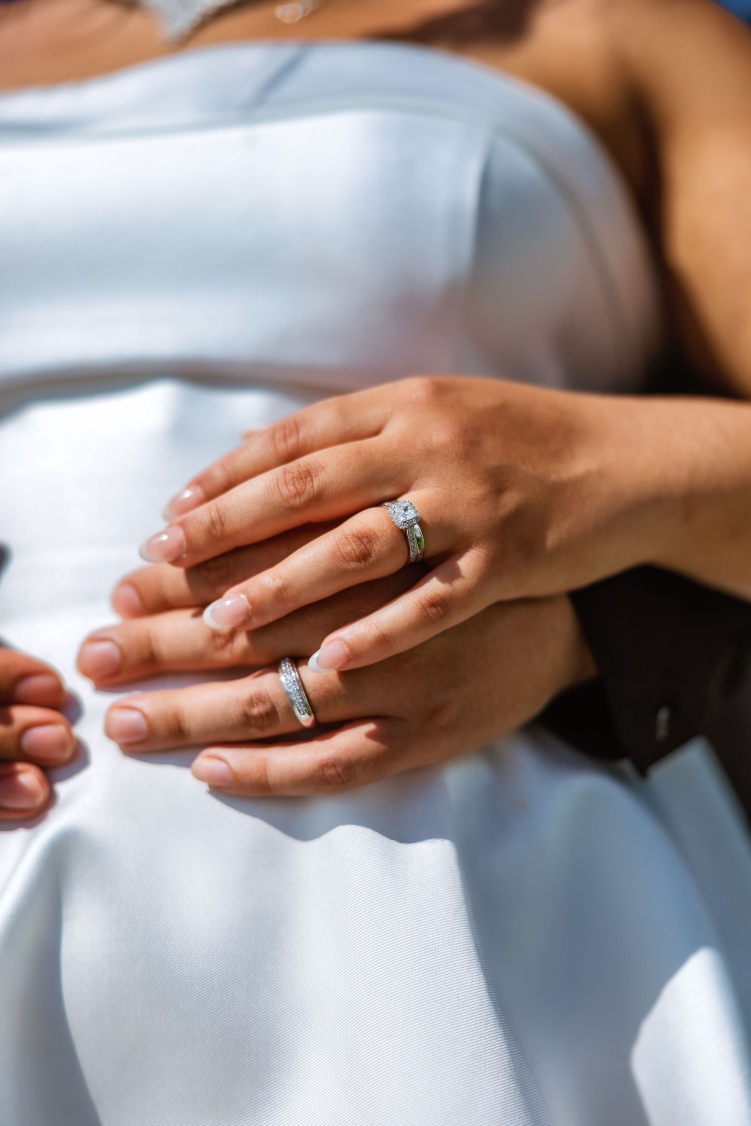 Close-up of bride and groom hands showing wedding rings, woman wearing diamond engagement ring and band.
