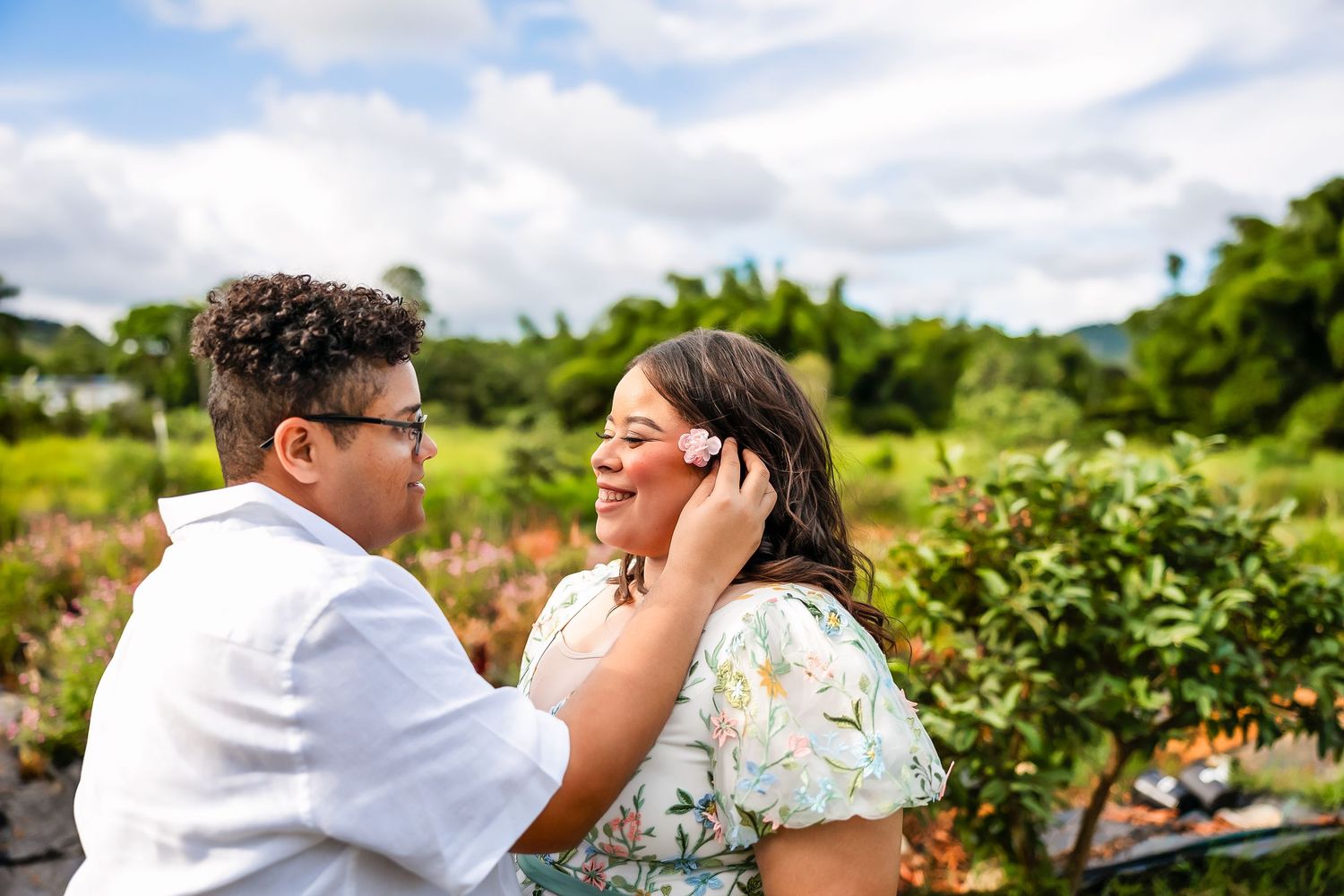 Couple sharing a tender moment outdoors, man gently touching woman's face in a lush green garden setting.