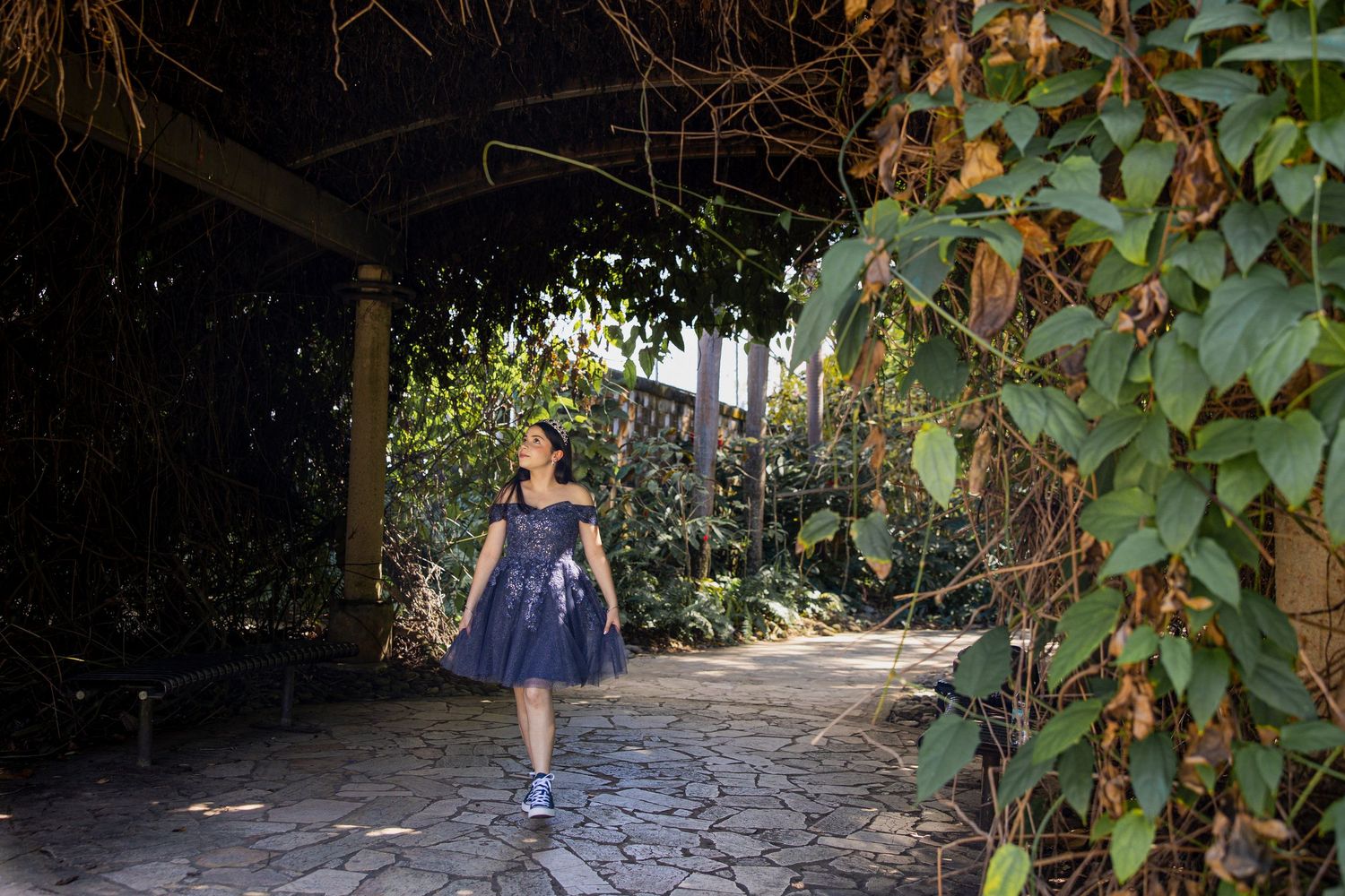 Person in dark blue dress walking through a vine-covered garden archway.