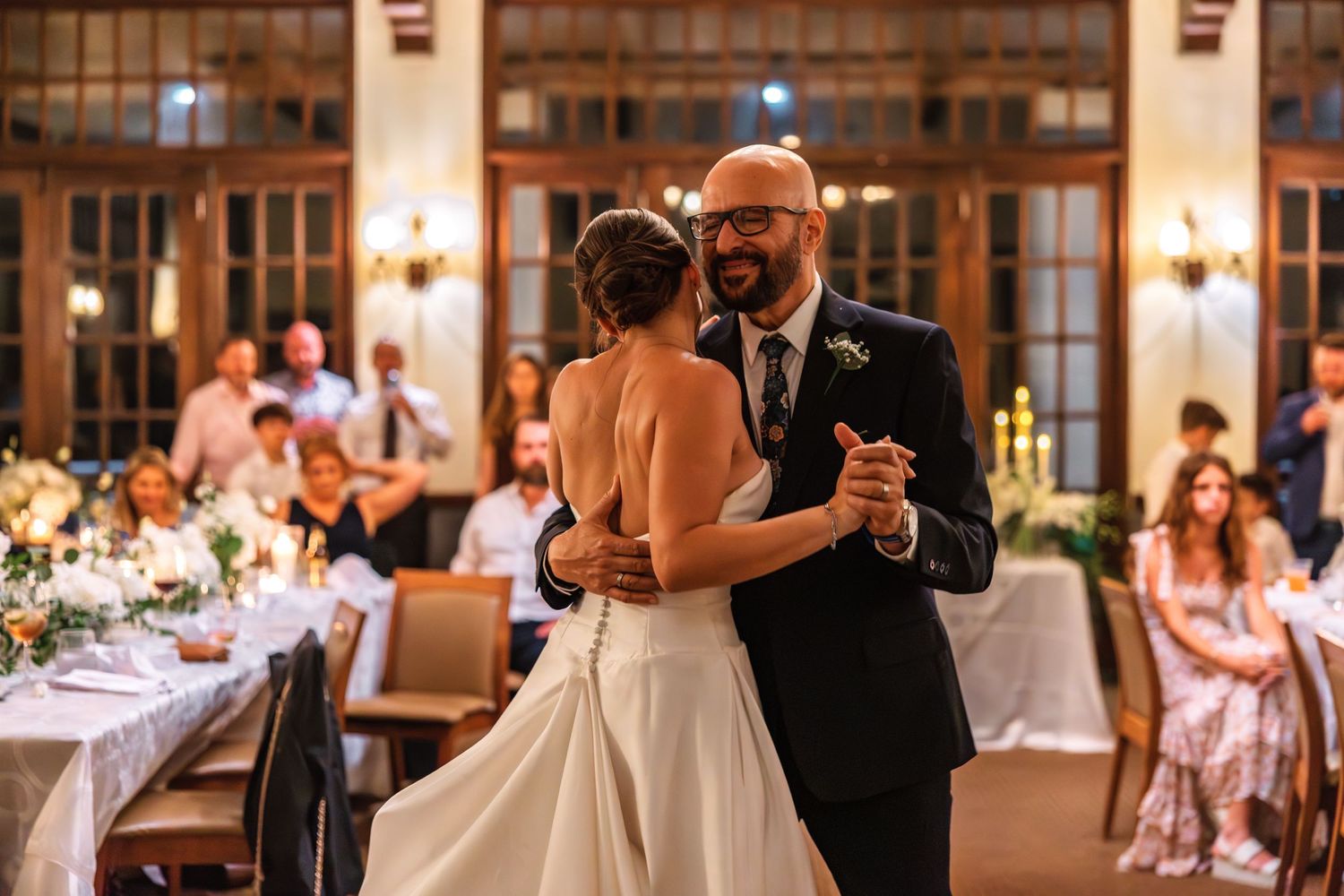 Bride and groom share their first dance at elegant wedding reception with guests watching in warmly lit venue.