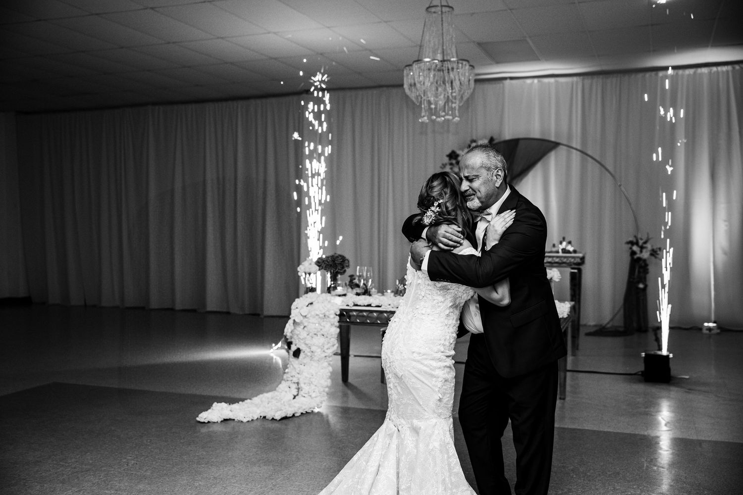 Black and white photo of bride and groom sharing first dance at wedding reception with sparkling fountains in background.