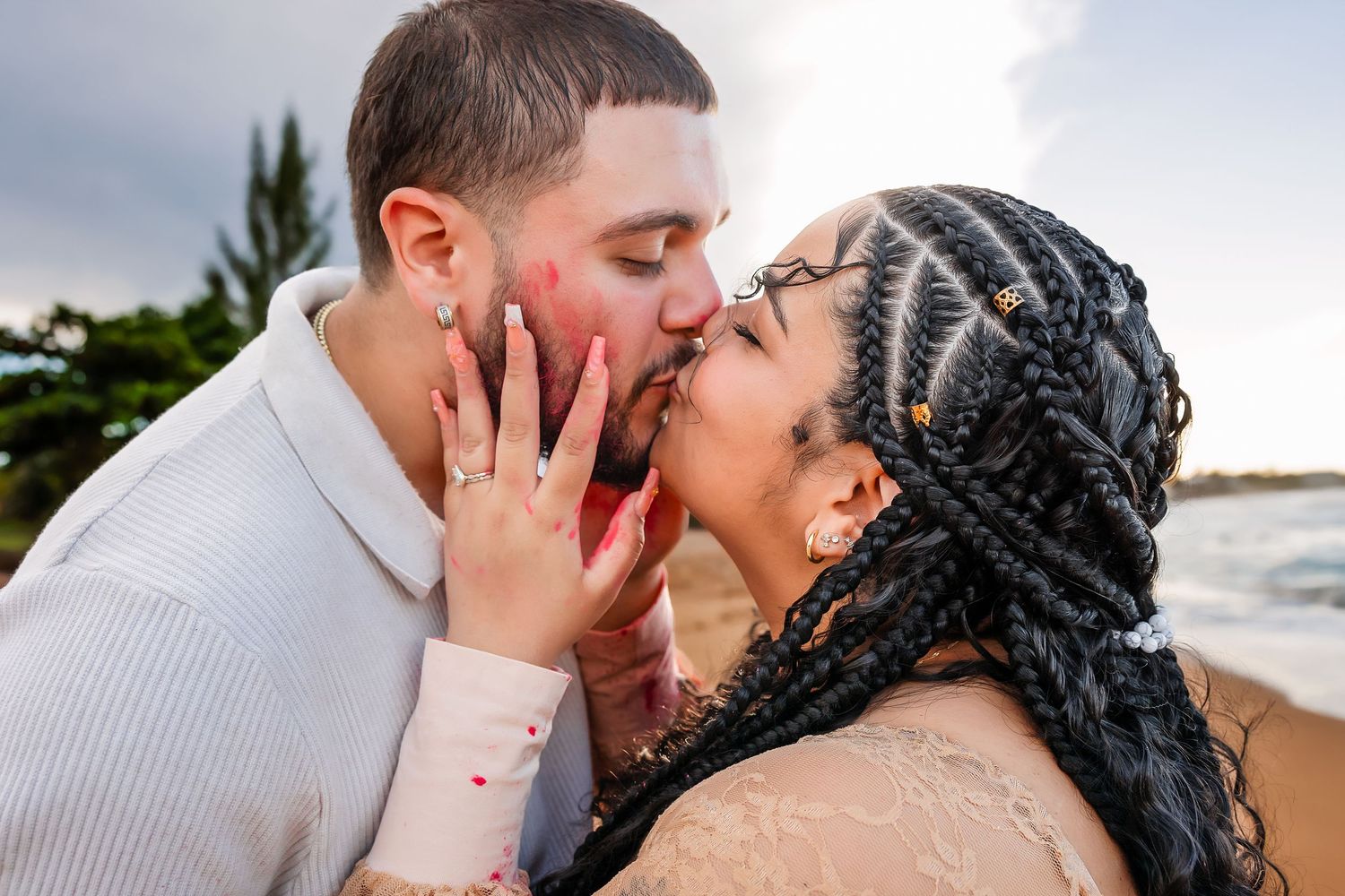 Couple sharing a romantic kiss on the beach, woman with braided hair in lace dress.