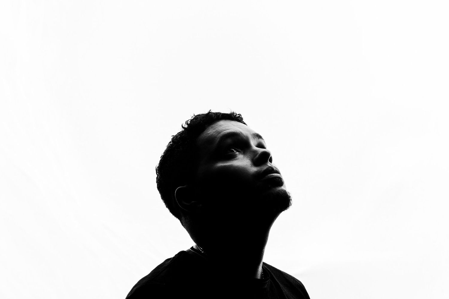 Black and white silhouette portrait of a young man looking upward against a bright white background.
